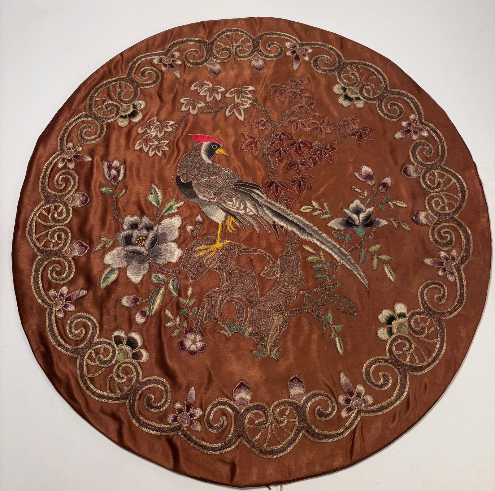 A Chinese embroidered silk roundel: Chinese embroidered silk roundel, Qing dynasty, late 19th century. The circular panel depicts a bird perched on a flowering branch, surrounded by a scrolling floral border, all finely worked in polych