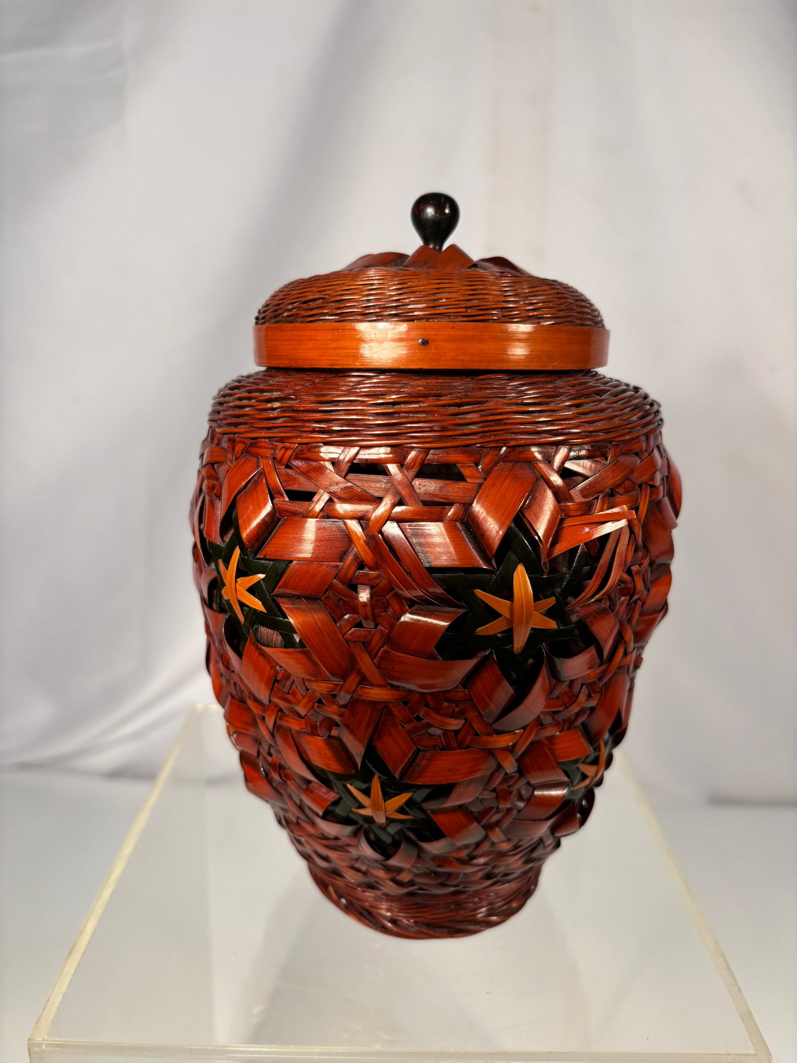 Japanese Woven Bamboo/Rattan Basket-Form Lidded Jar with Yellow Glazed Ceramic Liner: A finely woven cylindrical basket in a rich reddish-brown lacquered bamboo or rattan, decorated with a repeating star/flower motif in black and gold-toned splint work — likely a form of maki or dyed