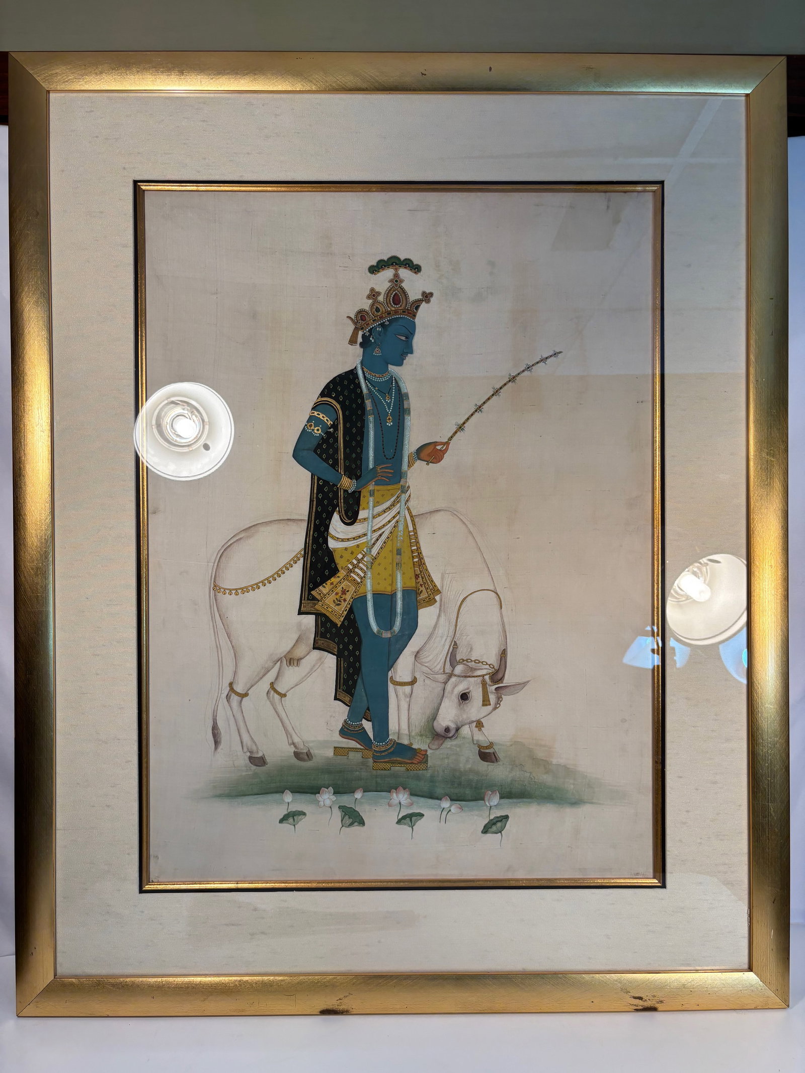 A Large Indian Painting of Krishna with Cow (Govinda); Gouache on Paper: 19th century; Opaque watercolor and gold on paper; Depicting Krishna in his traditional blue form, standing adorned with elaborate jewels, necklaces, and a richly patterned yellow and black robe, crow