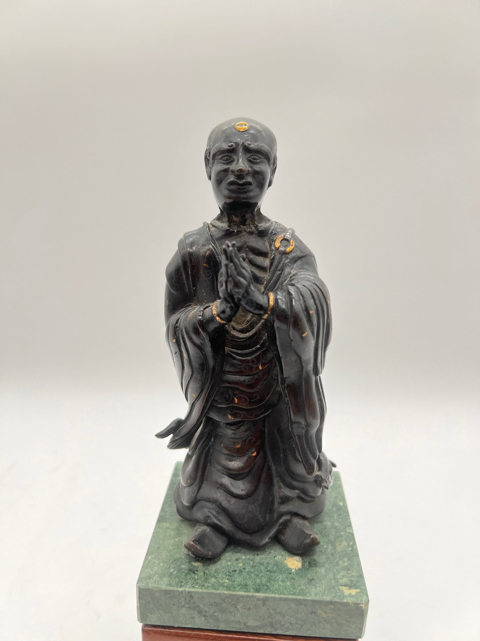 A Japanese silver inlaid gilt bronze monk statue with marble vase: 19th century ; The statue depicted in the images appears to be a bronze or brass figure of a Buddhist monk or an enlightened being (arhat or luohan). The statue has silver inlaid and gilt on the bronz