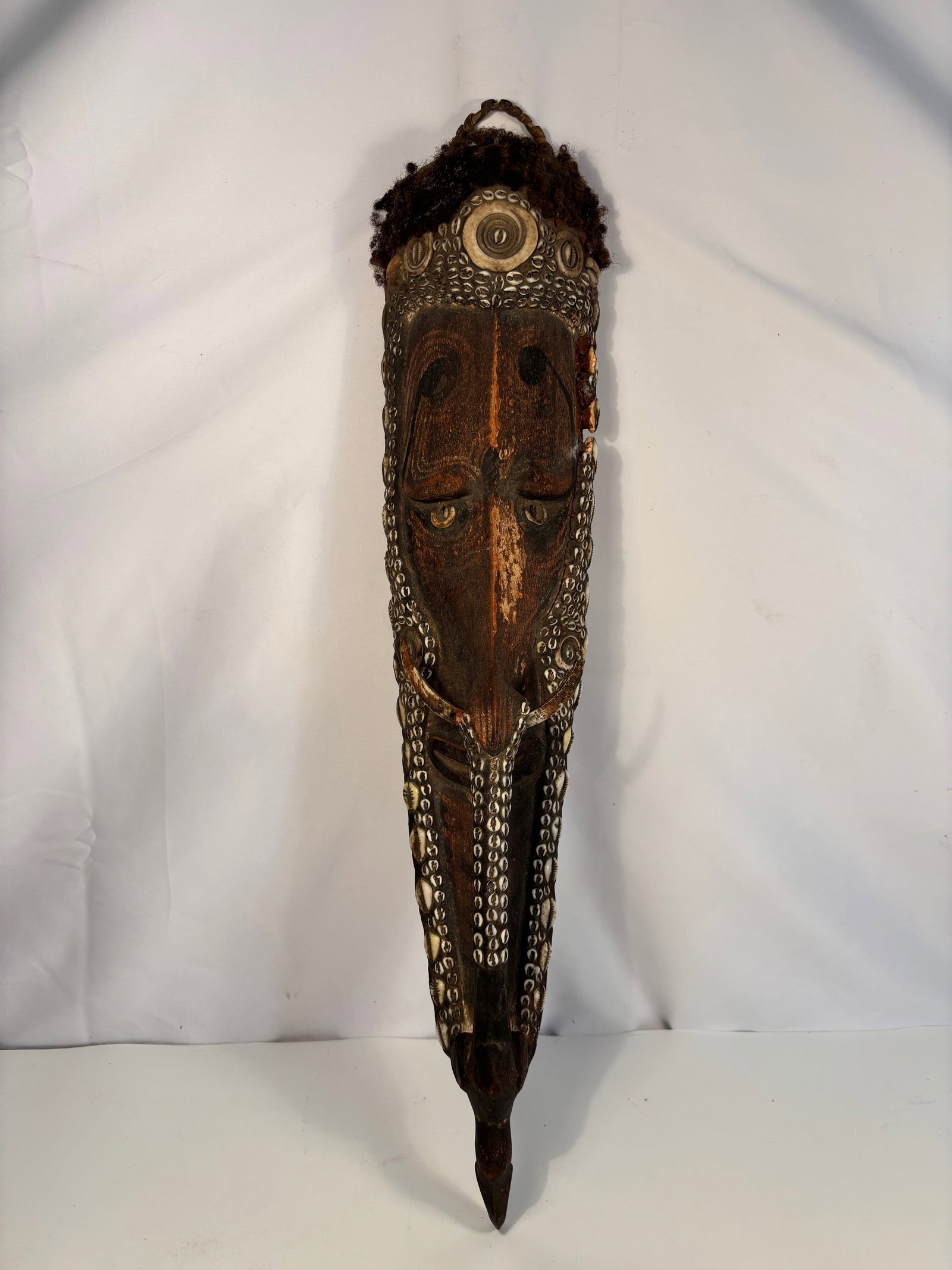 Papua New Guinea Cowrie-Shell Adorned Wooden Mask, Sepik River Region: Early to Mid 20th century ; A finely carved wooden ceremonial mask from the Sepik River region of Papua New Guinea, richly decorated with rows of natural cowrie shells along the contours of the face. 