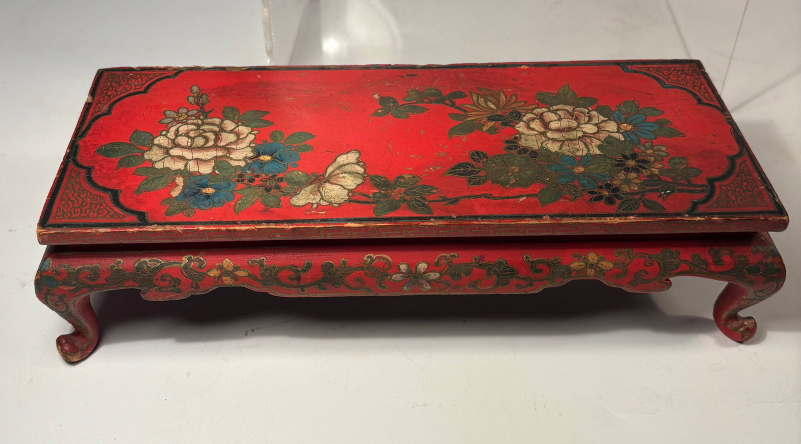 A Chinese Red Lacquer Painted Wooden Table Stand with Floral Decoration: Qing dynasty(1644-1912); Of rectangular form raised on four inward-curving legs with scrolled feet, the surface finely decorated with hand-painted peony blossoms and foliage in shades of green, white,