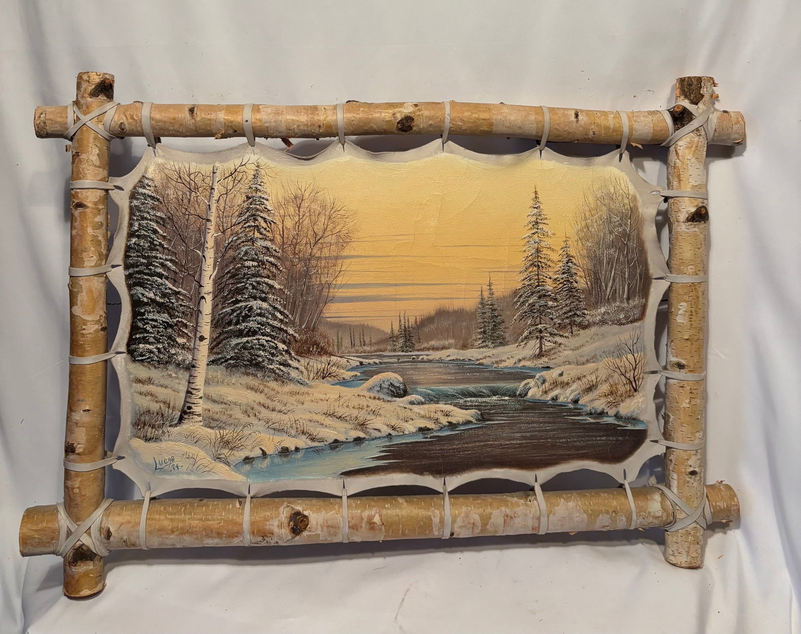 Lucas Signed Winter Landscape on Hide, Dated 1974, 32 x 20 In.: Hand-painted winter landscape on natural hide, signed “Lucas” and dated 1974. Depicting a snow-covered river scene with birch and evergreen trees. Mounted in a rustic birch log frame. A classi