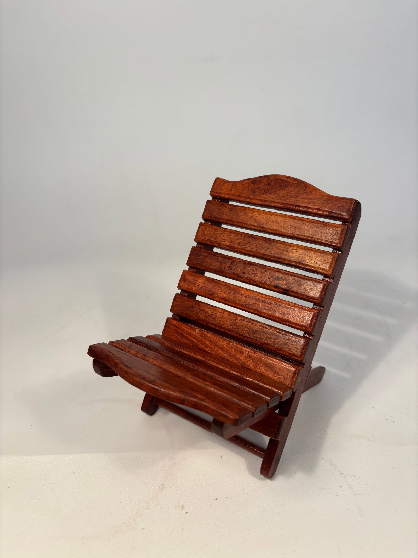 A Miniature Chinese Huanghuali/ rosewood Folding Chair, Scholar’s Model: A miniature Chinese-style folding lounge chair, finely crafted from richly grained hardwood, likely huanghuali or similar dense tropical wood. The chair features slatted construction with a gently arc
