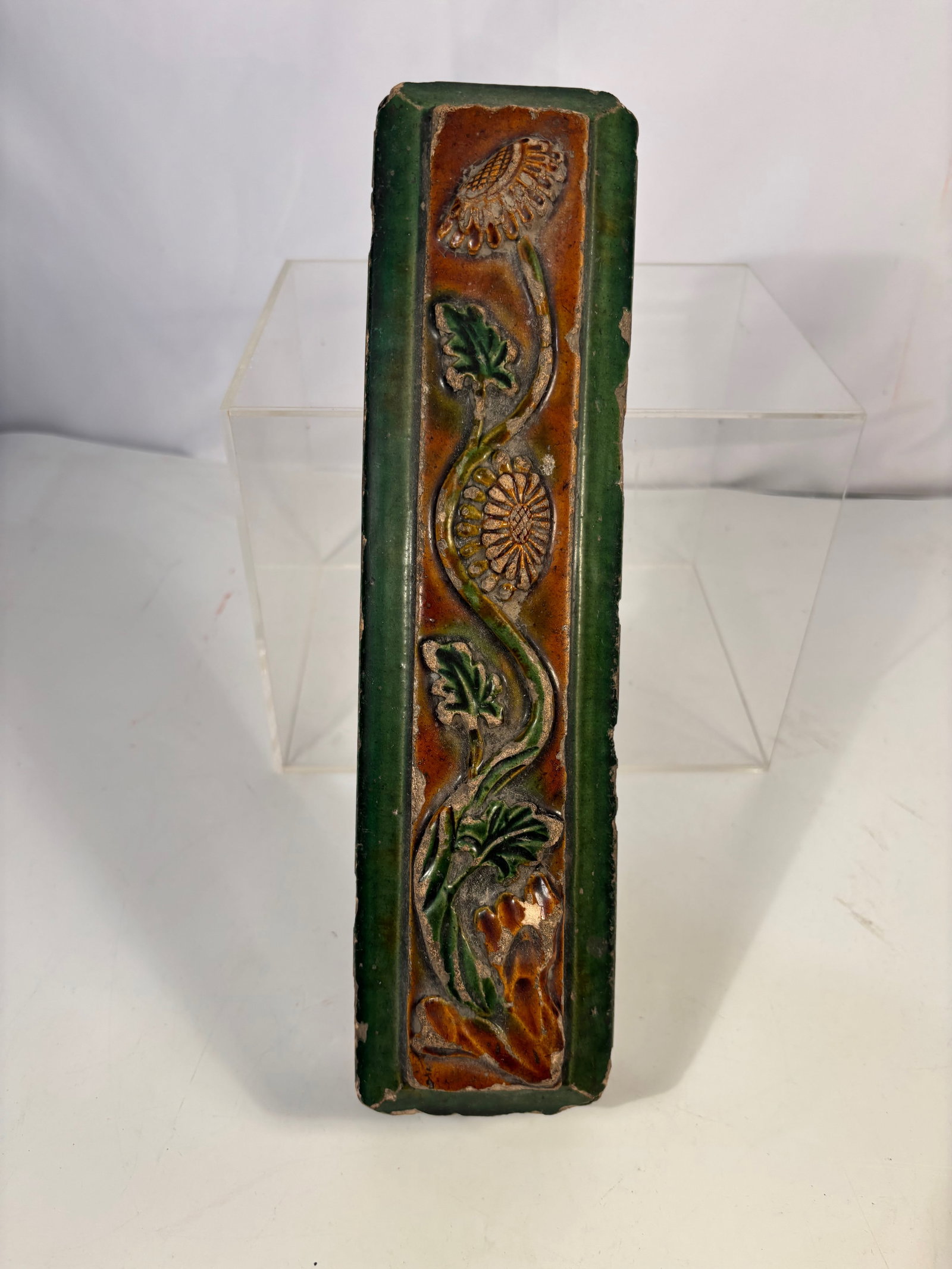 A Chinese Sancai-Glazed Relief Architectural Tile Panel , possibly 16-17th Century: Chinese sancai-glazed architectural tile decorated in raised relief with a stylized floral motif. The rectangular panel features green and amber-brown lead glazes surrounding a central flowering vine 
