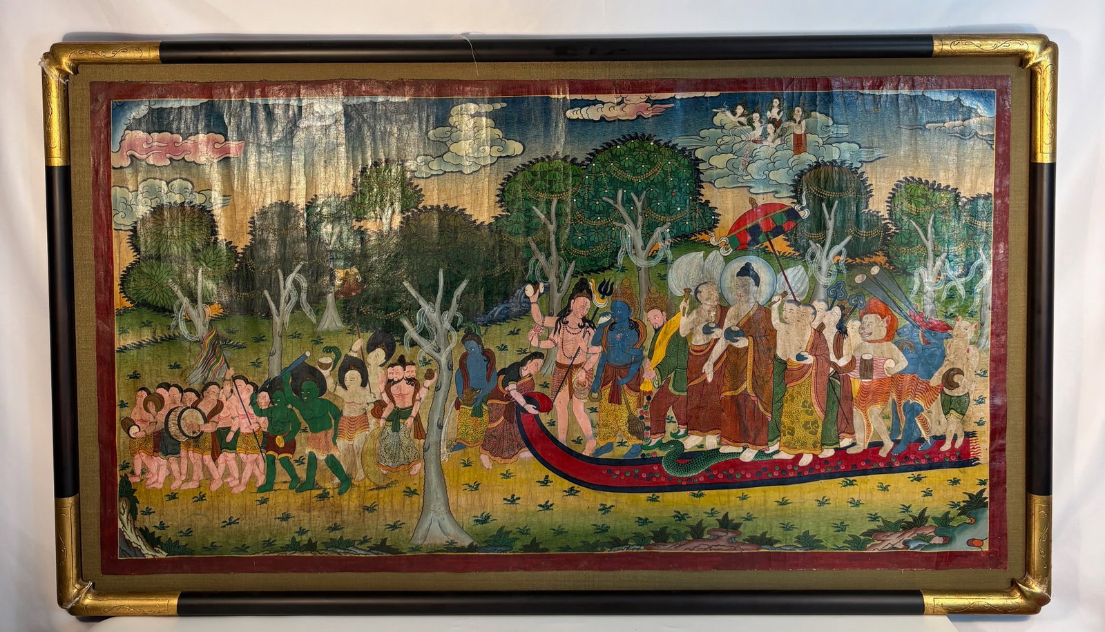 Thai/Burmese/Nepalese Buddhist Painting on Canvas “Buddha Crossing the River: 19th Century; A vibrant Buddhist painting on canvas, depicting the Buddha with disciples crossing a river under a parasol, accompanied by attendants bearing offerings. Celestial musicians appear amids