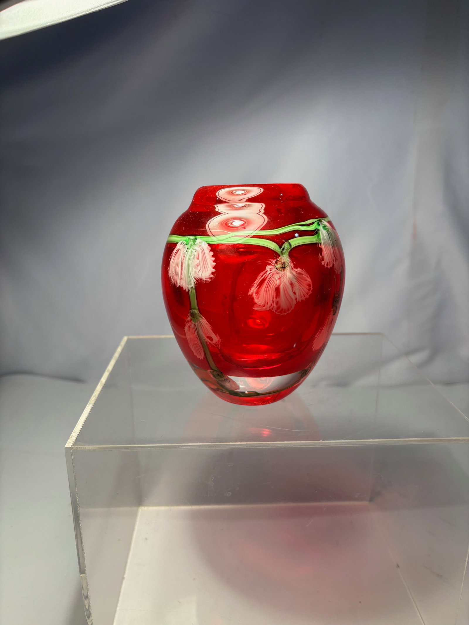 A Large Red Art Glass Vase with Applied Floral Garland Decoration: A substantial hand-blown art glass vase of rounded baluster form in rich translucent ruby red. Decorated with applied trailing green glass vines encircling the shoulder, suspending delicate white pull