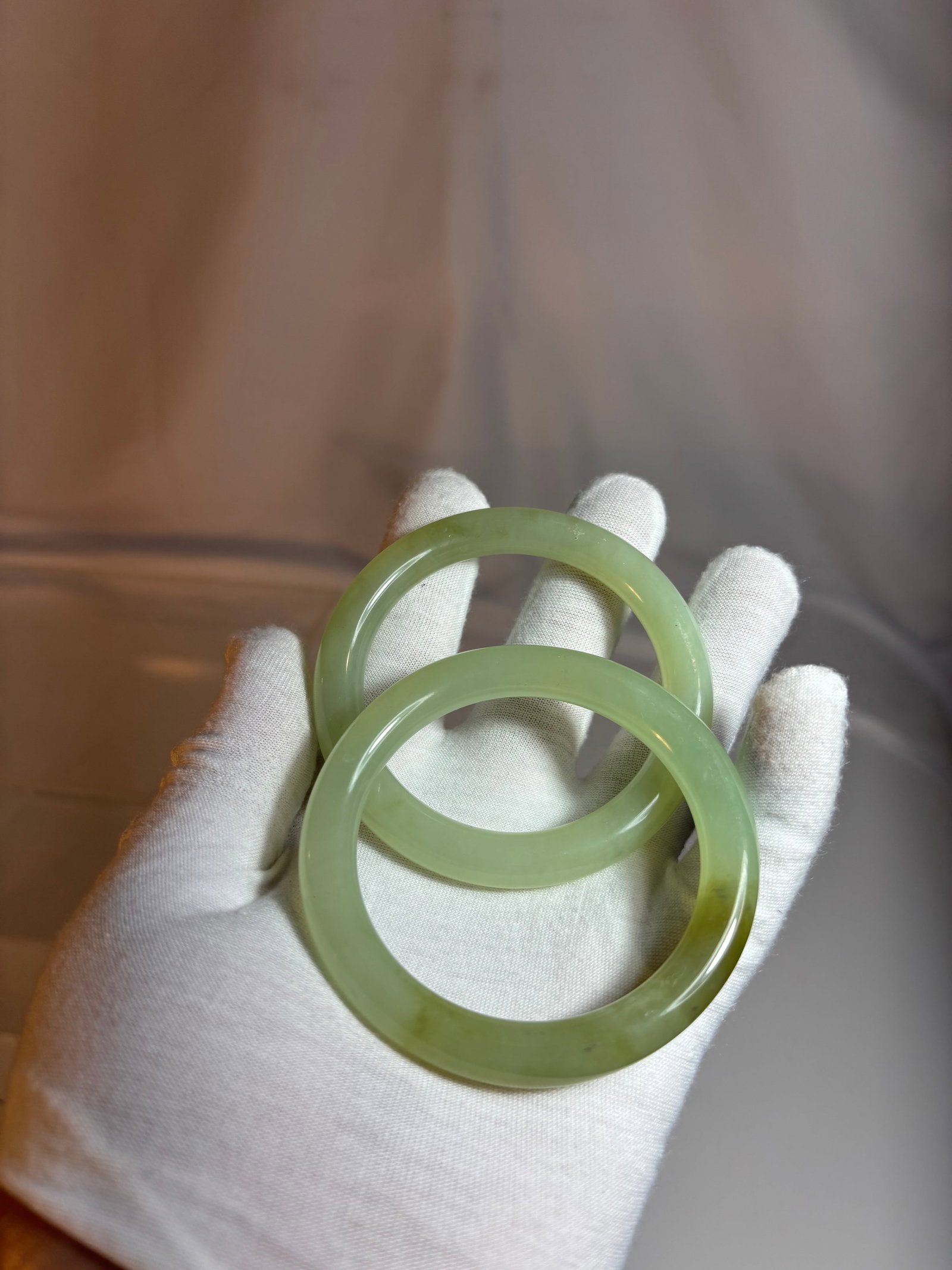 Pair of Chinese Jade Bangles: Pair of carved Chinese jade bangles in a soft yellow-green tone with semi-translucent appearance and polished finish. Each bracelet displays natural color variation and mottled inclusions characterist