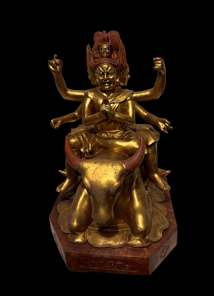 A Tibetan Style hand carved Gilt sandalwood Multi-Head Deity Figure: Tibetan-style hand carved Gilt sandalwood gilt figure depicting a multi-headed, multi-armed wrathful deity seated on a recumbent bull, features expressive faces, dynamic posture, and detailed sculptur