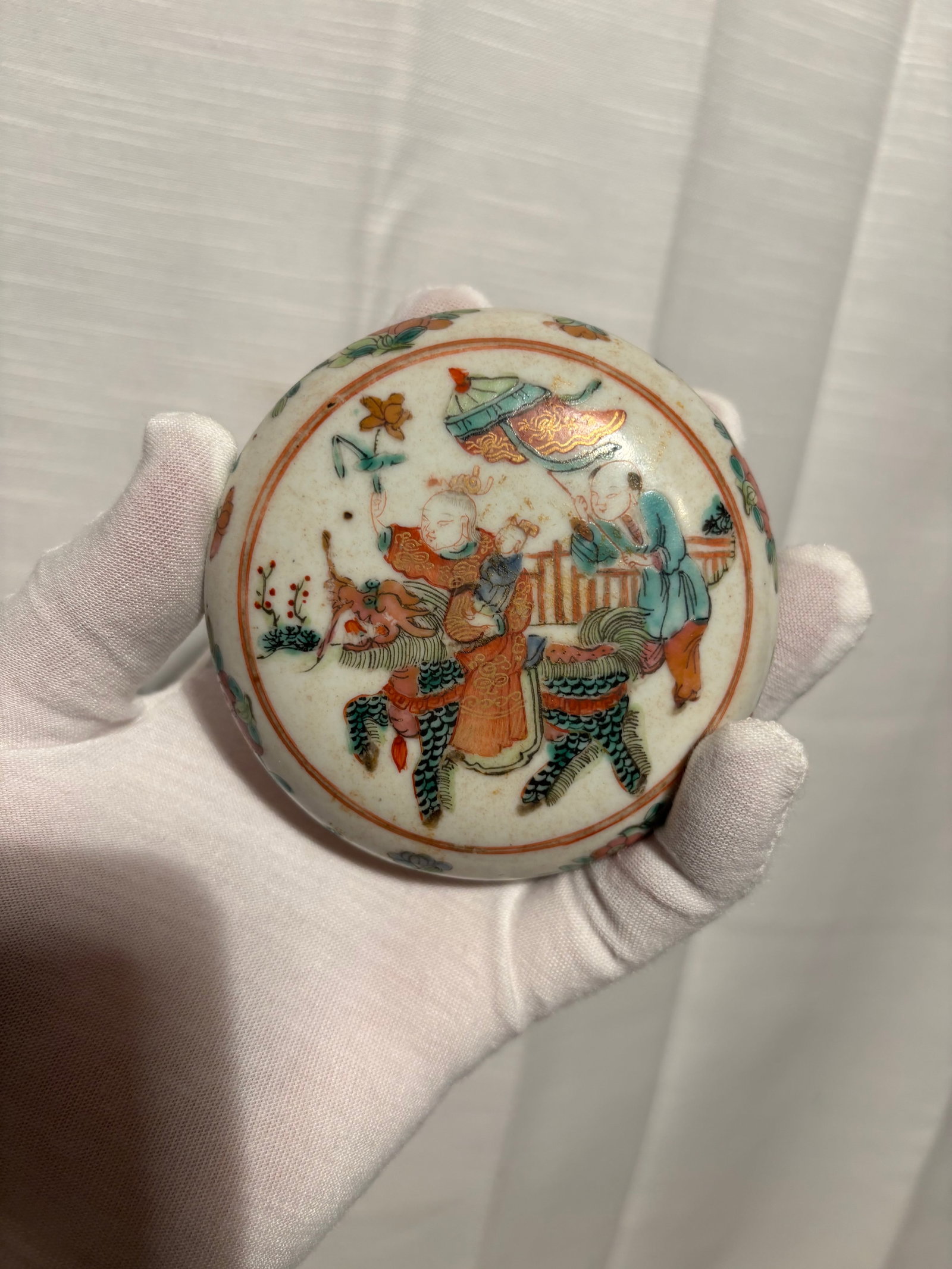 A Chinese Famille Rose Enamel Porcelain Covered Box, Figural Scene: Qing Dynasty(1644-1912); A Chinese porcelain covered box decorated in famille rose enamels, featuring a central figural medallion scene of figures in a garden setting. The domed lid is finely hand-pai