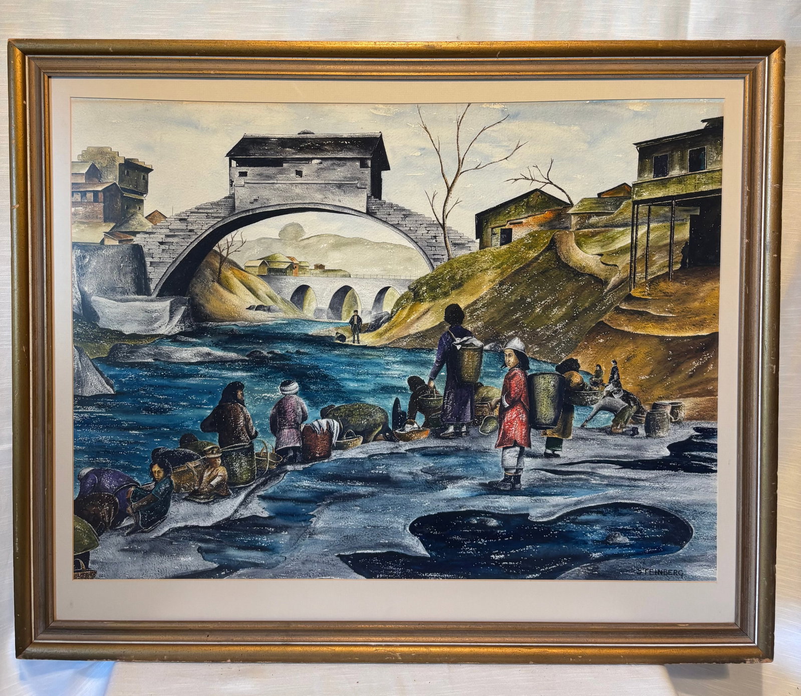 Steinberg (20th Century), Village River Scene with Figures and Bridge, Framed Painting: A detailed and visually engaging painting depicting a village riverside scene with figures gathered along a flowing stream beneath a large arched bridge. The composition is rich with narrative element