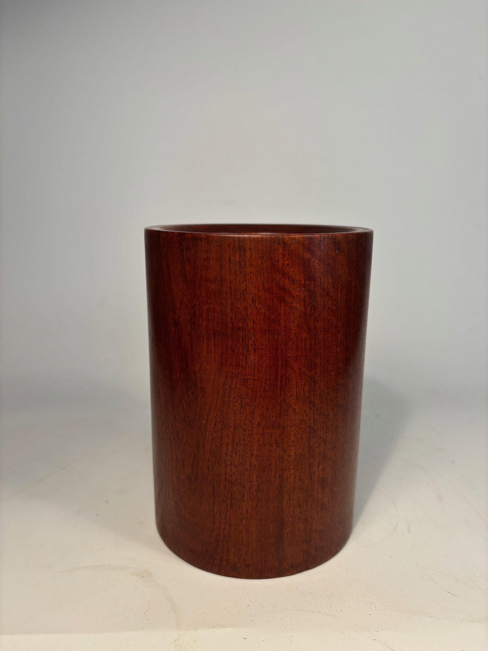A Chinese Huanghuali/ rosewood Brush Pot: A finely crafted Chinese cylindrical brush pot (bitong), made from dense, richly grained huanghuali/ similar rosewood, with a subtle taper and smooth-polished surface showcasing the vibrant honey-to-c