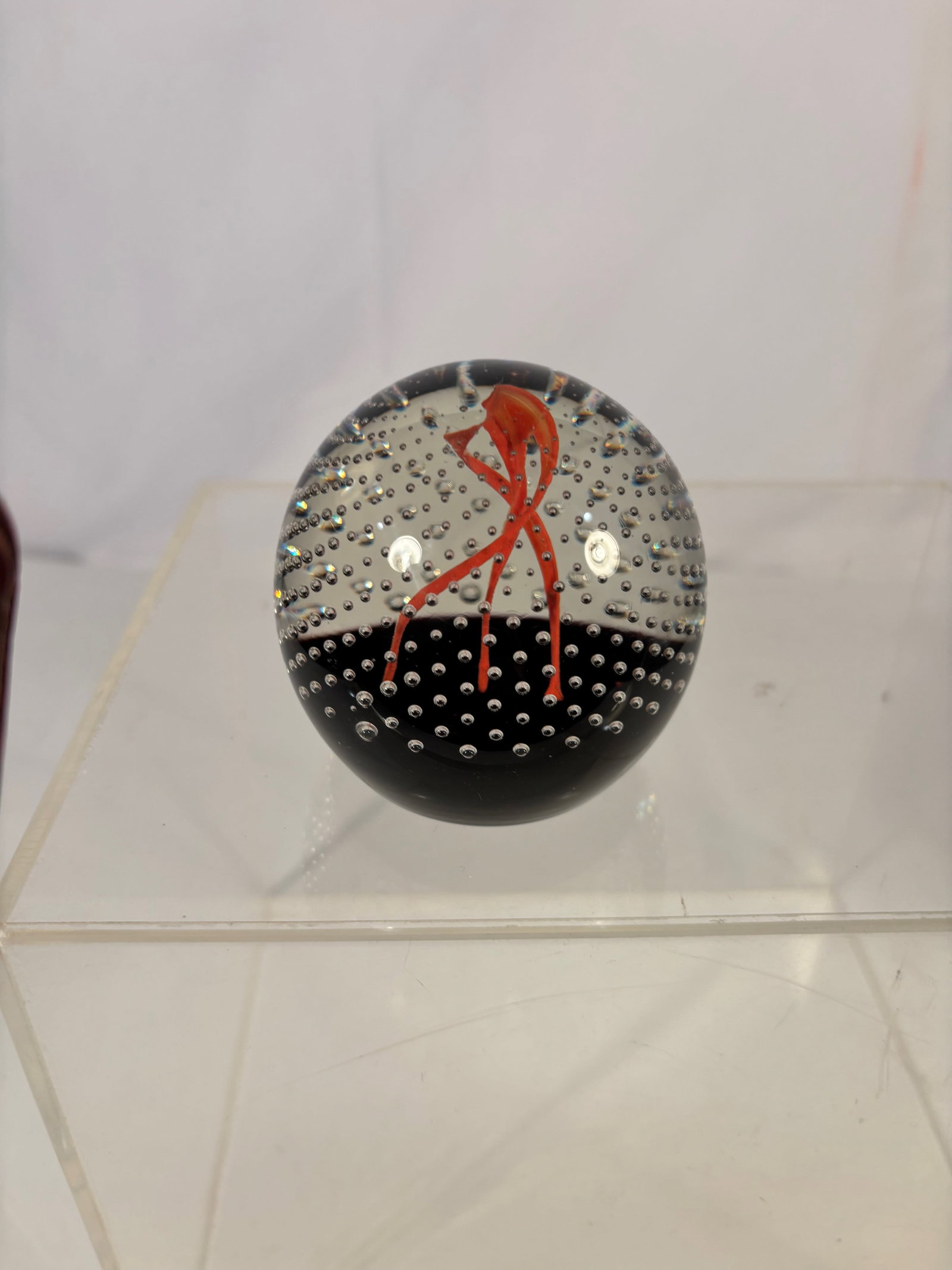 An Art Glass Paperweight with Red Ribbon and Controlled Bubble Ground: Art glass paperweight featuring an abstract flowing red ribbon form suspended within a clear dome over a black ground. The interior is decorated with dense controlled air bubbles, creating a dynamic, 