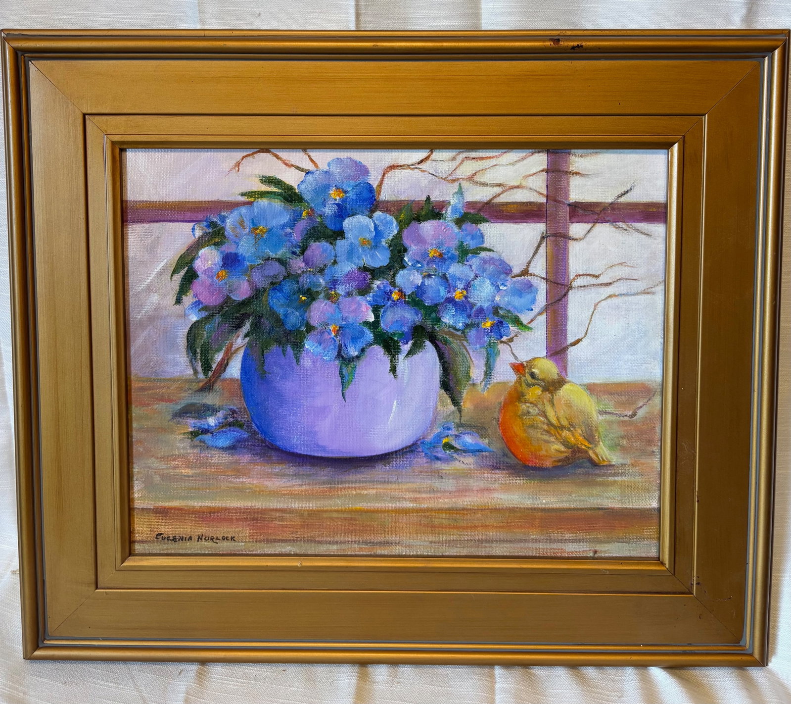 Eugenia Lawson Norlock (American) Floral Still Life with Bird, Signed: An original still life painting by American artist Eugenia Lawson Norlock, depicting a vibrant arrangement of blue and violet flowers in a rounded vase, accompanied by a small bird resting beside a pi