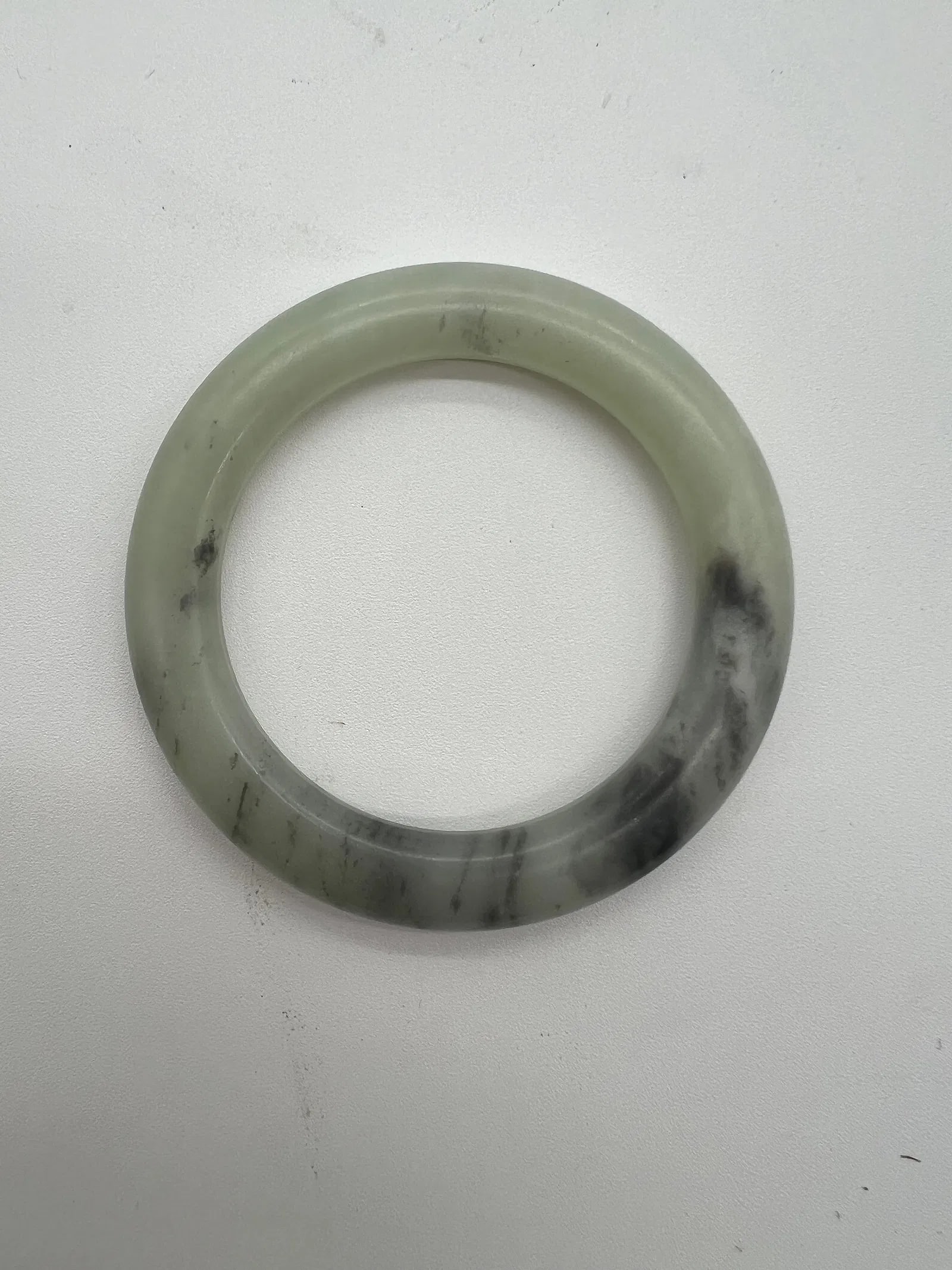 A Chinese “tire-shaped,?? nephrite jade bangle .: Qing dynasty (1644-1912); this jade bangle has a thick and rounded appearance. The bangle in the image has a predominantly light green or off-white base with some darker areas or spots. Dimensions?Thi