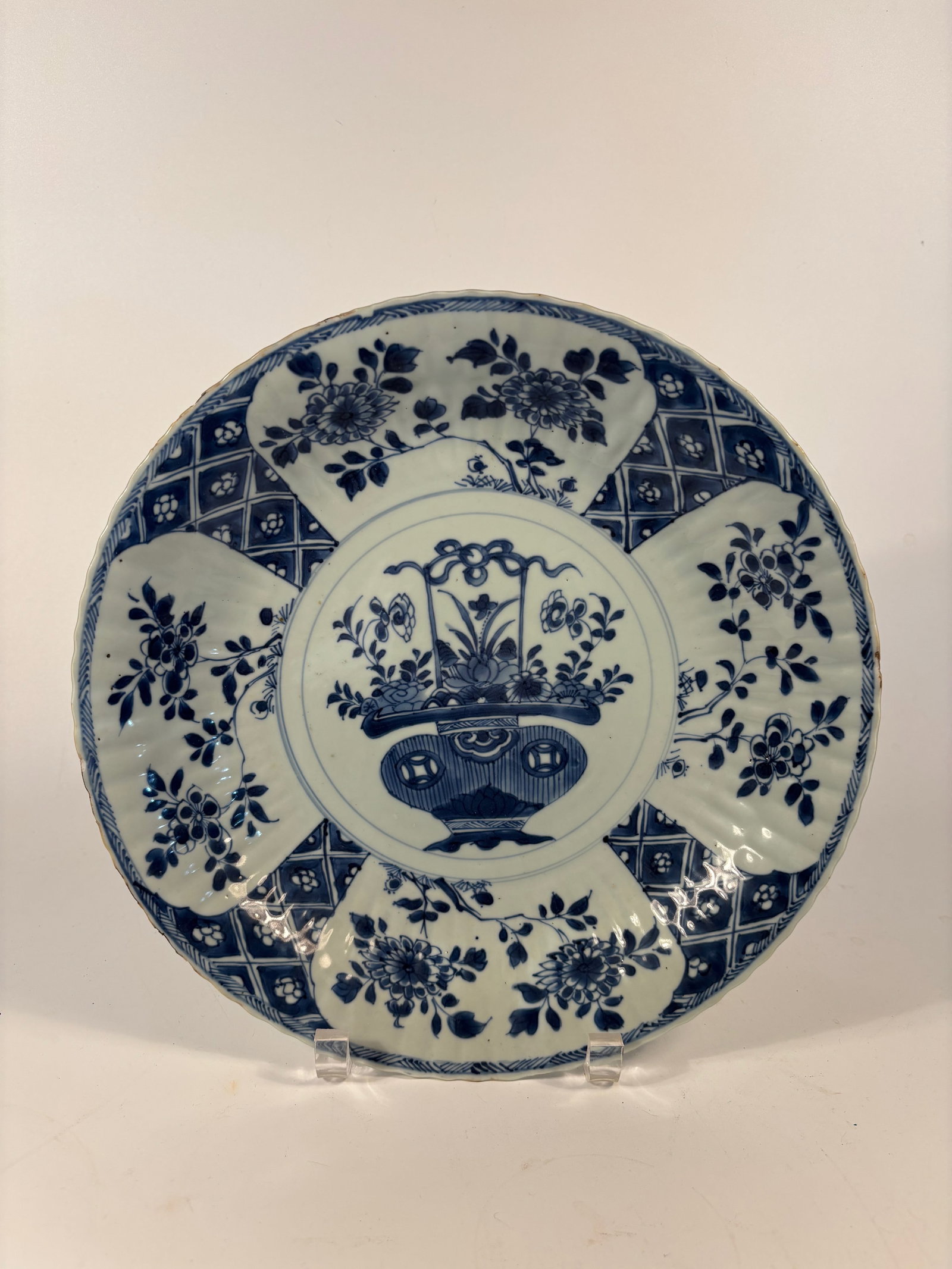 A Large Chinese blue and white porcelain plate: Kangxi (1662–1722), Central flower basket motif, symbolizing prosperity and abundance.Four outer reserves with floral sprays alternating with lattice diaper patterns.Classic cobalt blue underglaze d