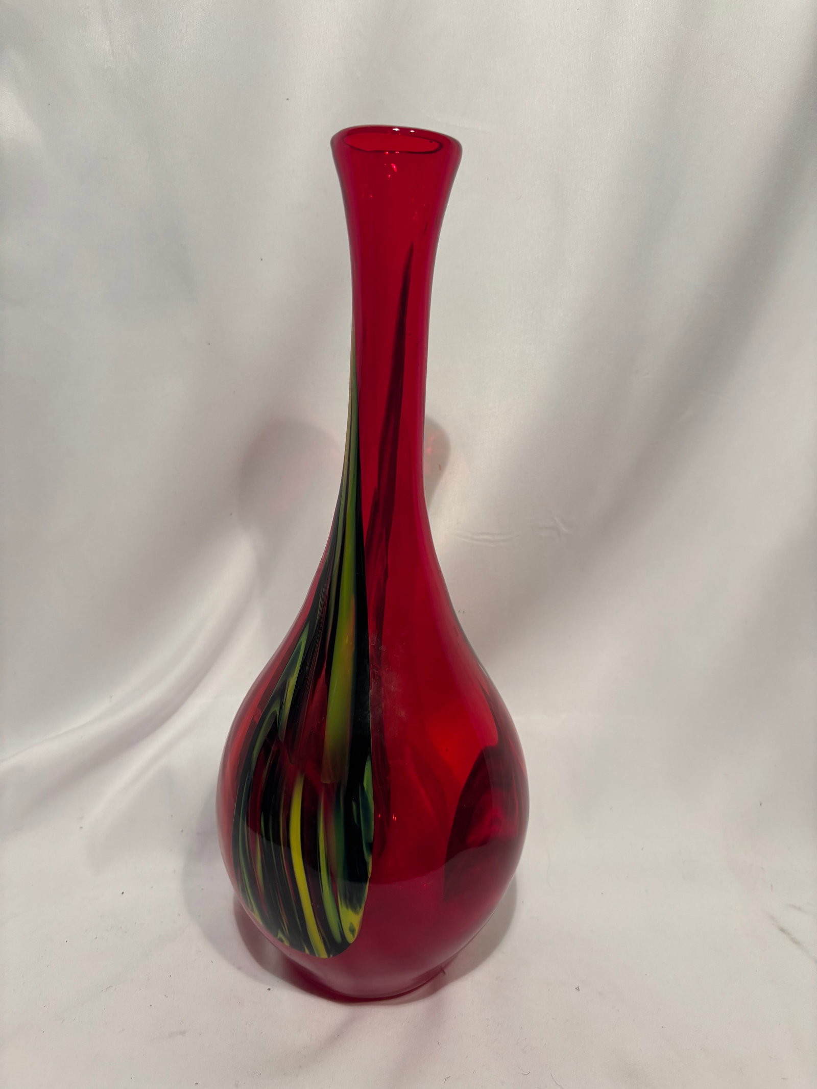 Vintage Murano Style Ruby Red Art Glass Bud Vase: Hand-blown art glass vase of elongated baluster form, executed in translucent ruby-red glass with flowing green, yellow, and dark internal decoration. The vase displays a sleek modernist silhouette an