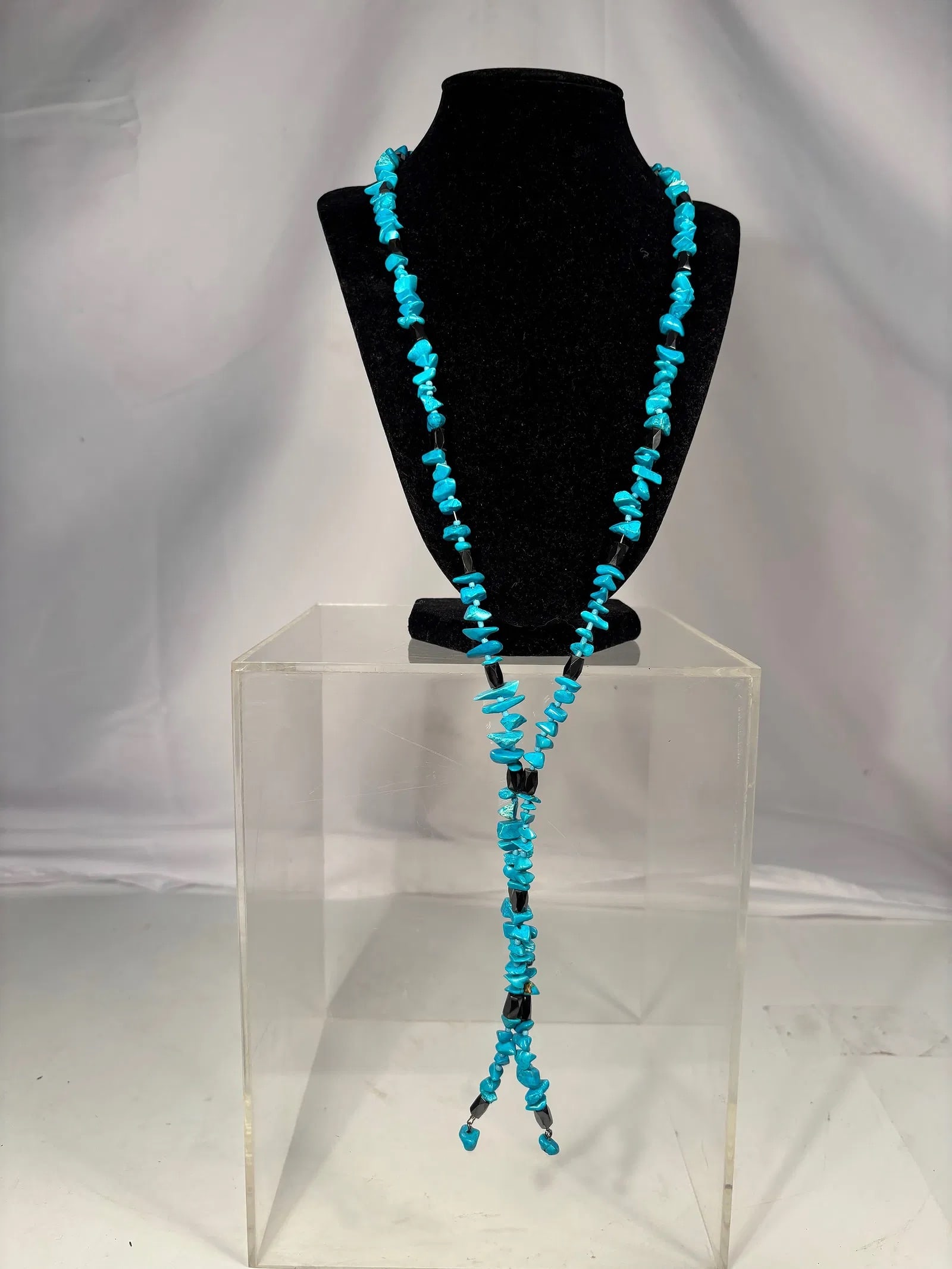 Long Turquoise Chip Stone Necklace with Magnetic Hematite Beads: Long necklace composed of turquoise chip stones separated by magnetic hematite beads. The necklace features vibrant blue coloration and a lariat-style design with decorative black accent beads through