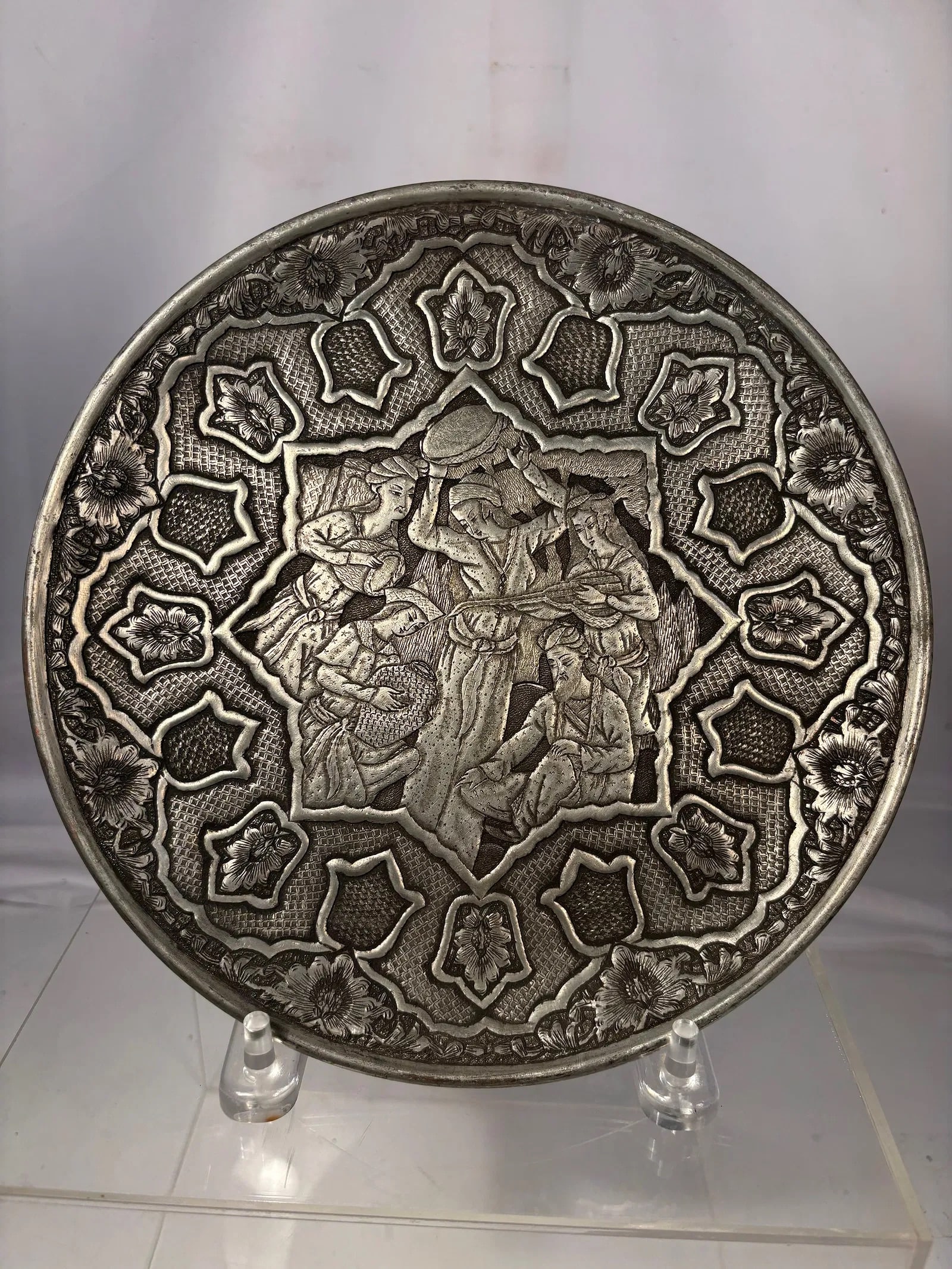 Hand-Engraved Persian Isfahan Ghalamzani Silvered Copper Decorative Charger: Persian-style circular decorative plate featuring a central figural scene surrounded by geometric and floral motifs in relief. The design depicts several figures in traditional attire within a shaped 
