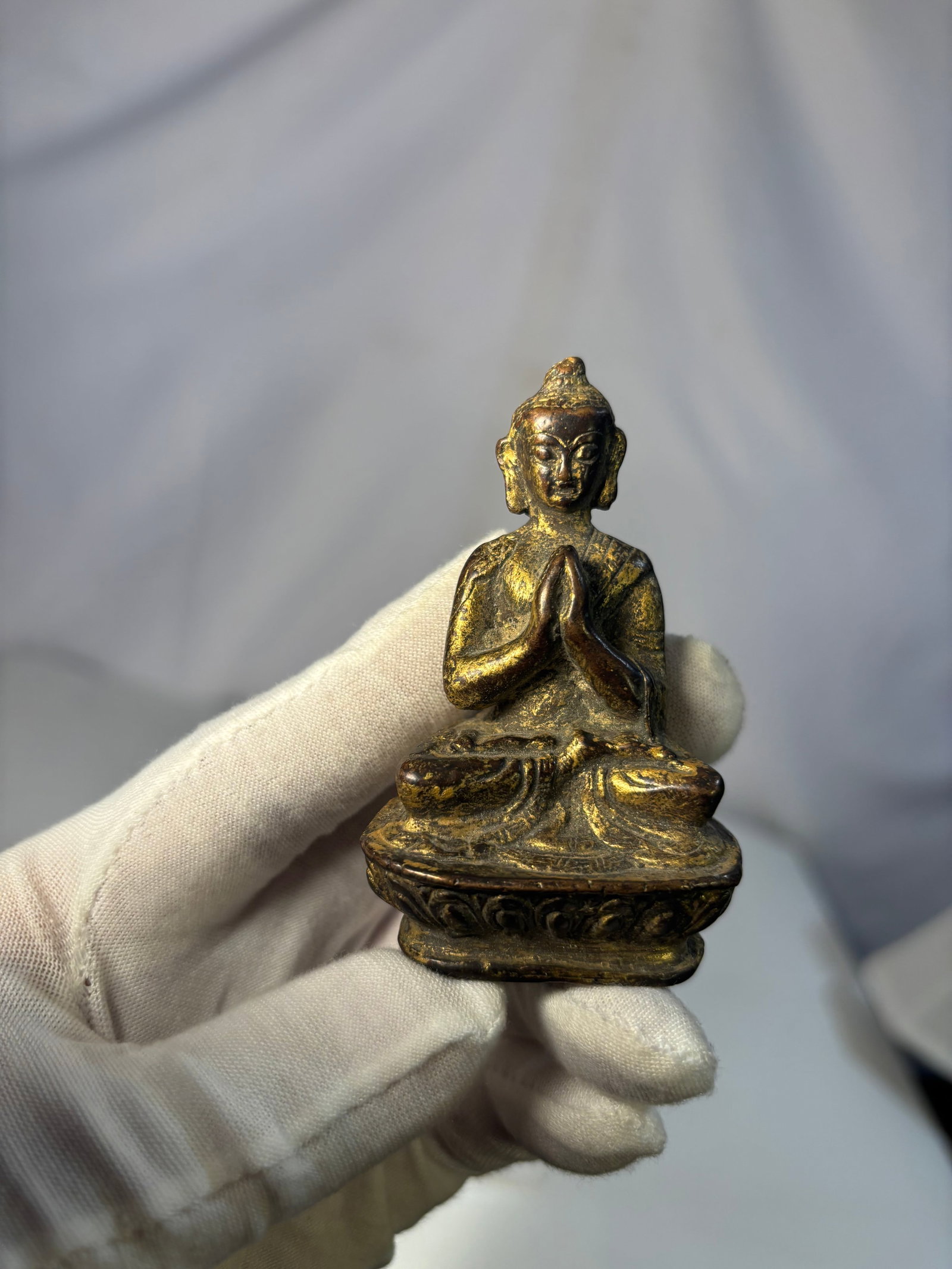 An Asian Gilt Bronze Seated Buddha Figure: A small gilt bronze figure of a seated Buddha, depicted in a meditative posture with hands held in añjali (prayer) mudra.The figure is cast with a serene facial expression, elongated earlobes, and a 