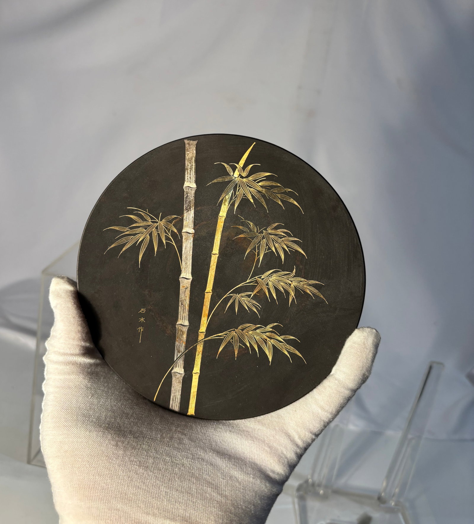 A Japanese Black-Patinated Metal Plate by Sekisui (???) with Gilt Bamboo: A Japanese black-patinated metal plate of rounded form, decorated with finely rendered bamboo in gilt against a dark ground. The design is executed with delicate engraved and gilded detail, highlighti