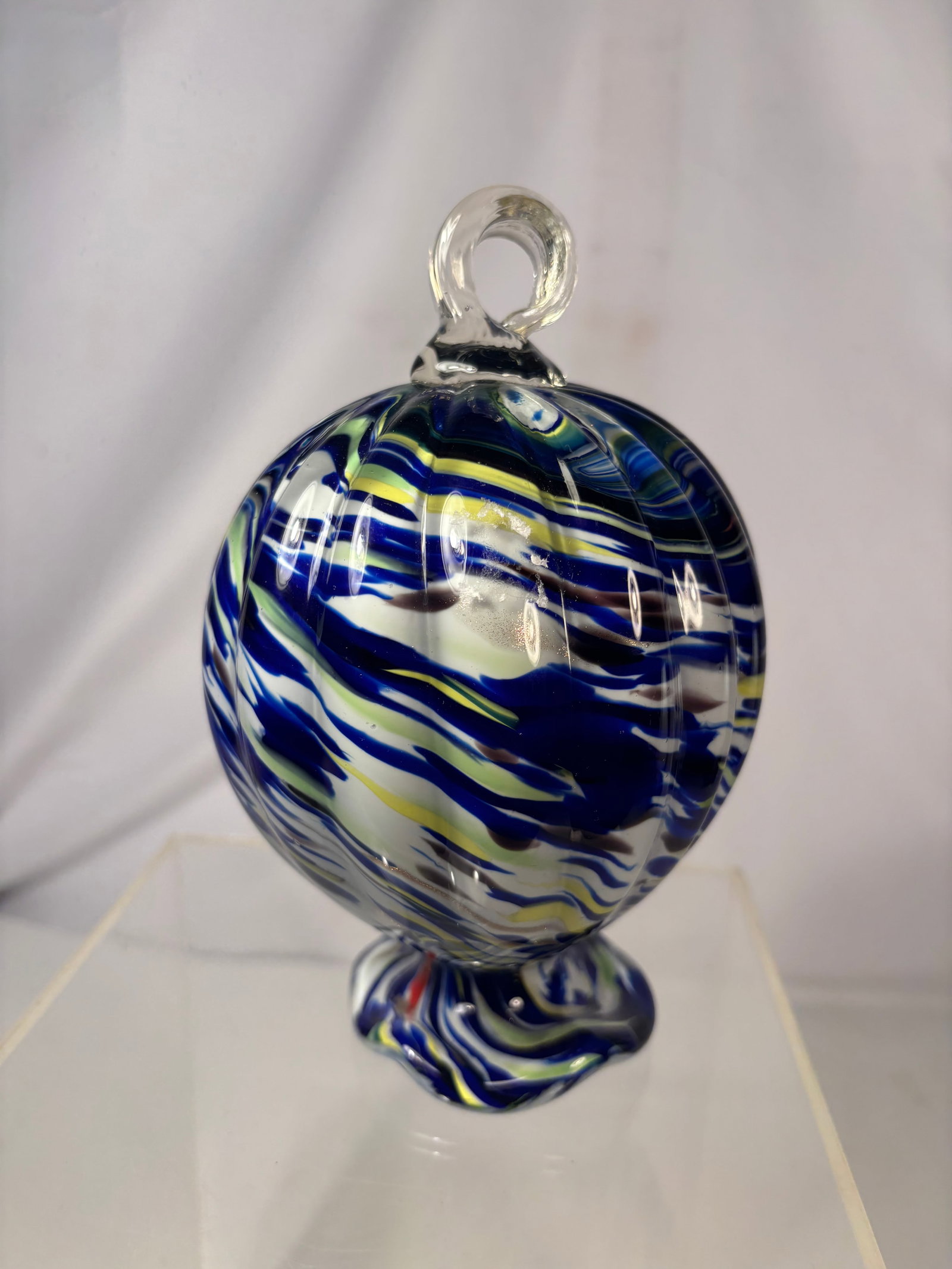 Vintage Hand-Blown Swirl Art Glass Orb Sculpture: A decorative hand-blown art glass orb featuring vivid cobalt blue, white, yellow, and red swirling ribbon patterns. Designed with a clear applied loop finial and a multicolored pedestal base. The unde
