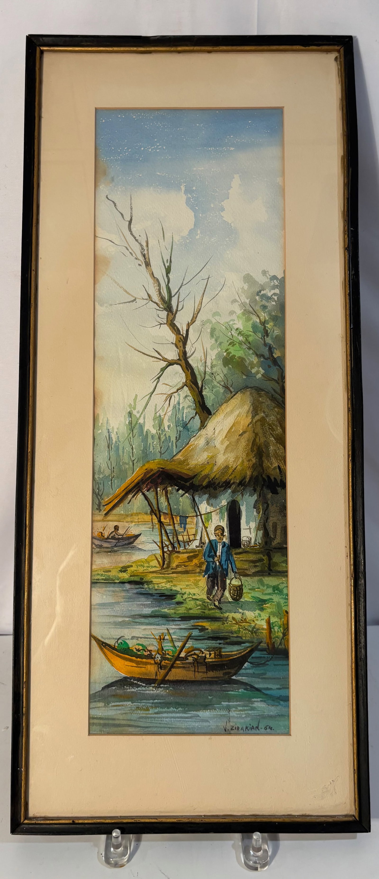 V. Zirakian (Iranian, 1940-), Framed Village Riverside Watercolor, Signed and Dated 1964: A charming watercolor on paper by V. Zirakian, signed and dated 1964 lower right. The composition depicts a peaceful riverside village scene with moored boats, a thatched cottage, and a standing figur