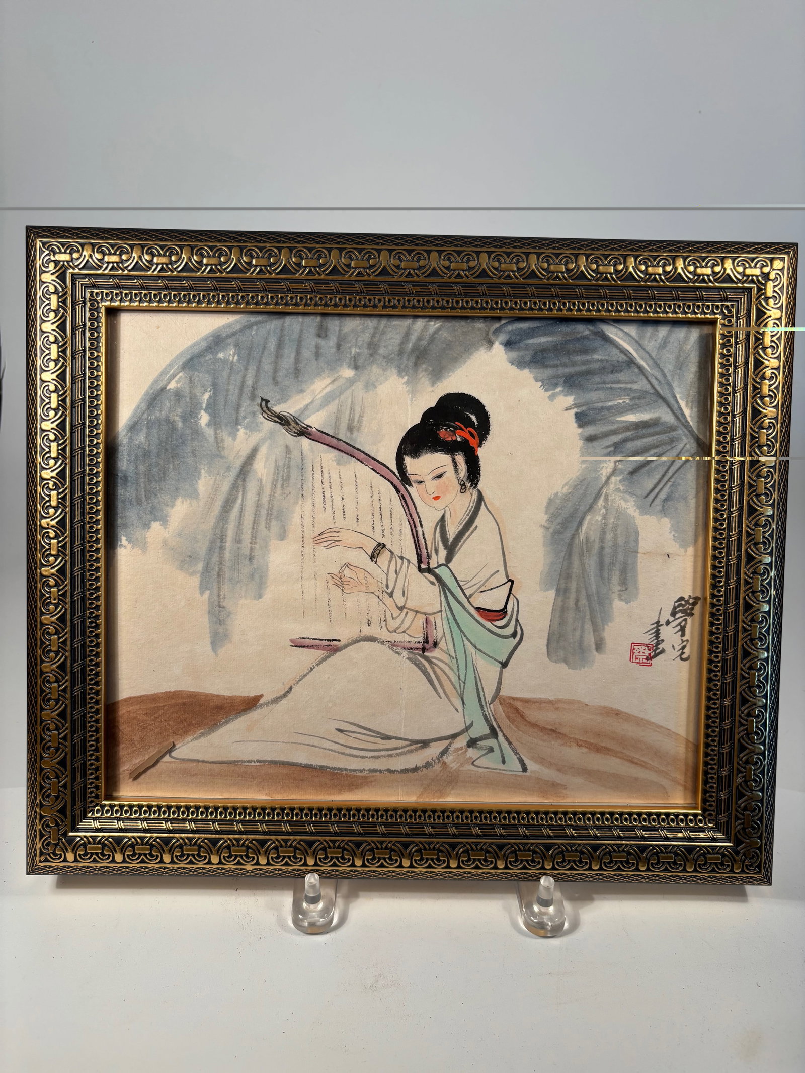 A Chinese Watercolor Painting signed by artist: A finely executed Chinese watercolor painting on paper, depicting a graceful lady seated beneath broad foliage, delicately playing instrument. The composition showcases elegant brushwork and subtle us