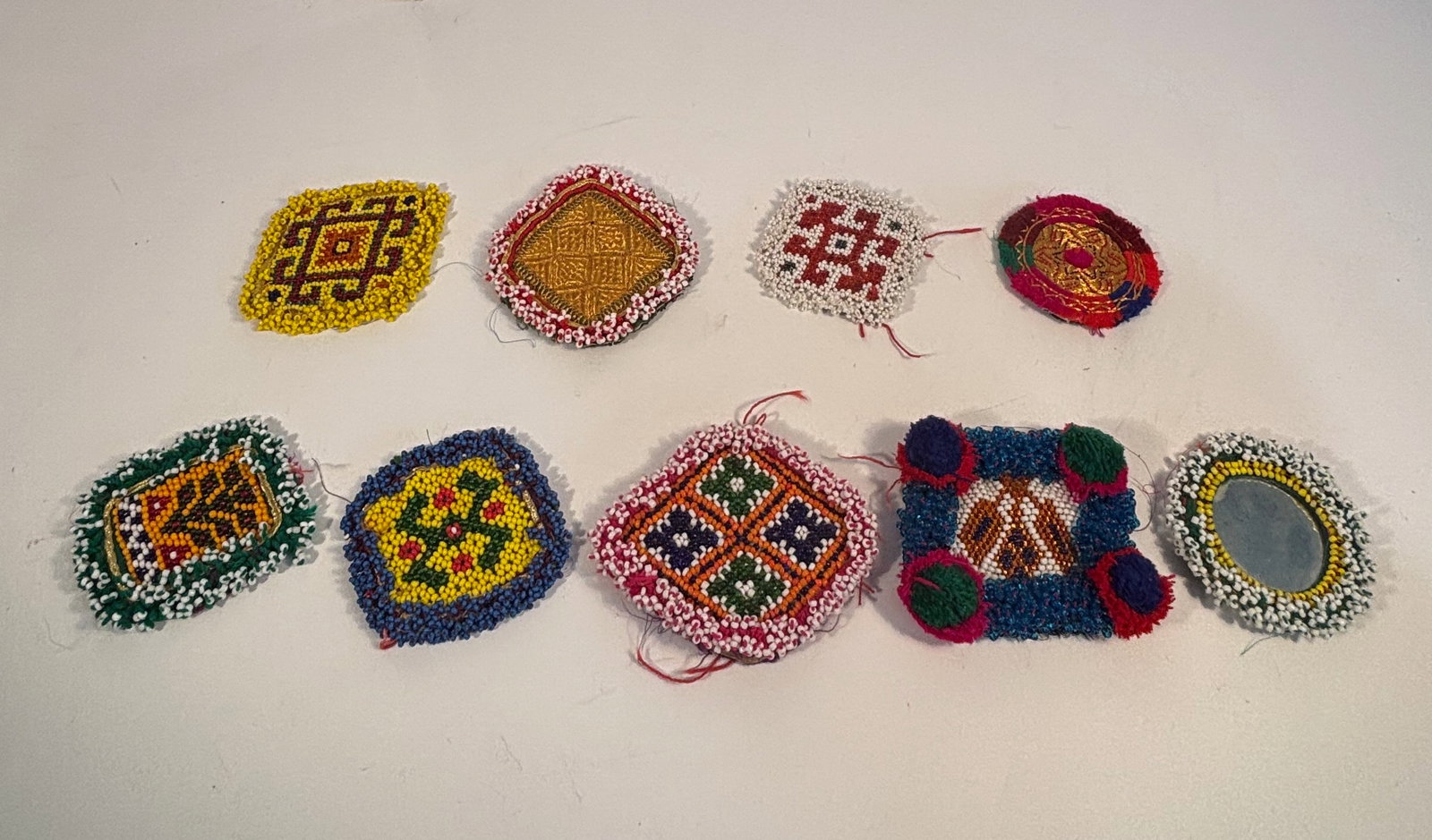 Lot of 9 Vintage Afghan/Pakistani Kuchi Hand-Beaded Tribal Medallions: A collection of nine vintage Kuchi tribal beaded medallions, also known as gul de peron (“dress flowers”) in Afghan Farsi. Each medallion is handmade with colorful glass seed beads and textile