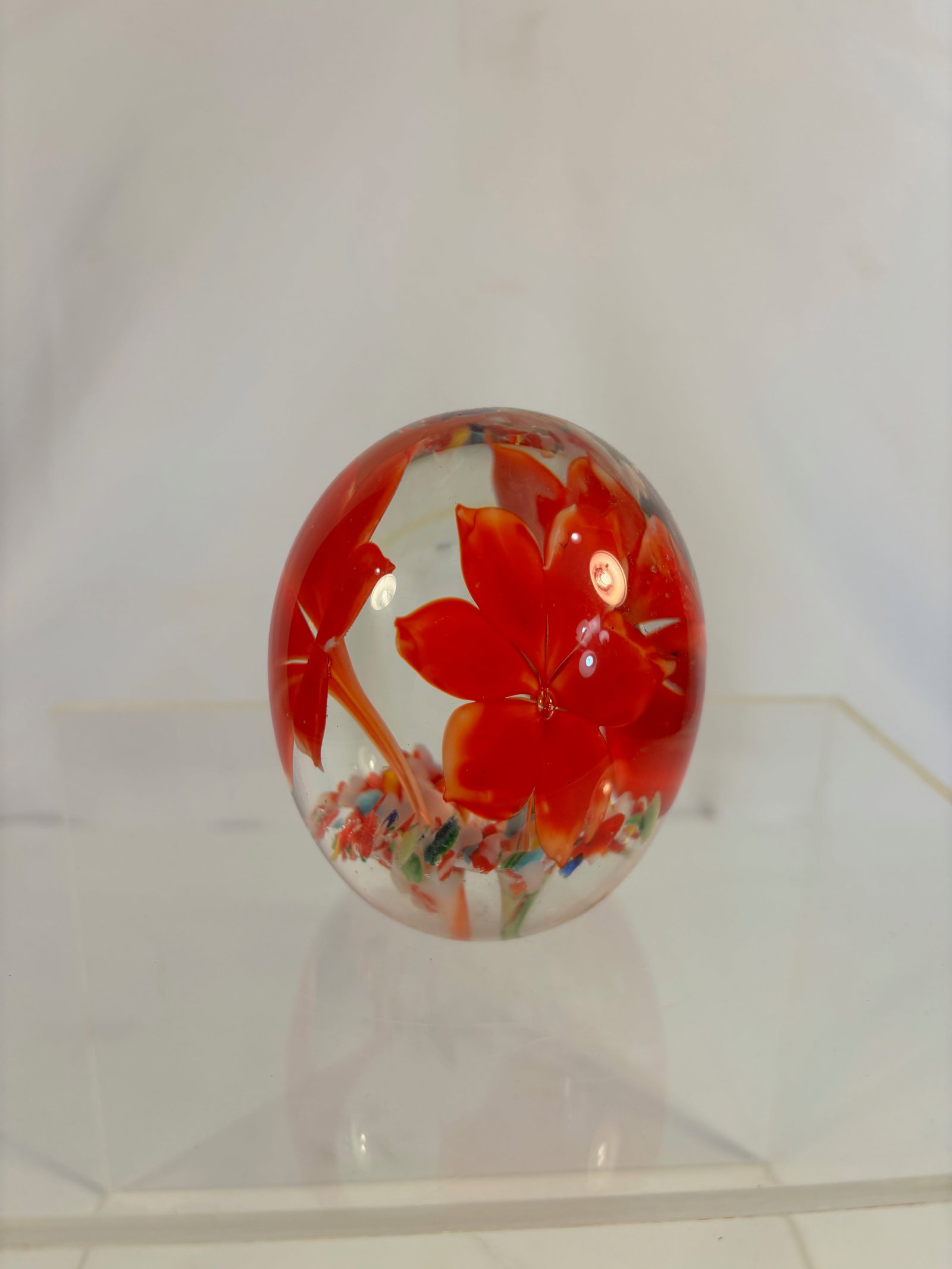 A Murano-Style Art Glass Floral Paperweight with Red-Orange Blossom and Multi-Color Base,: Brilliant clear glass paperweight encasing a vivid red-orange six-petal flower rising from a base of multicolored millefiori-like fragments. The bloom is skillfully lampworked with dimensional petals 