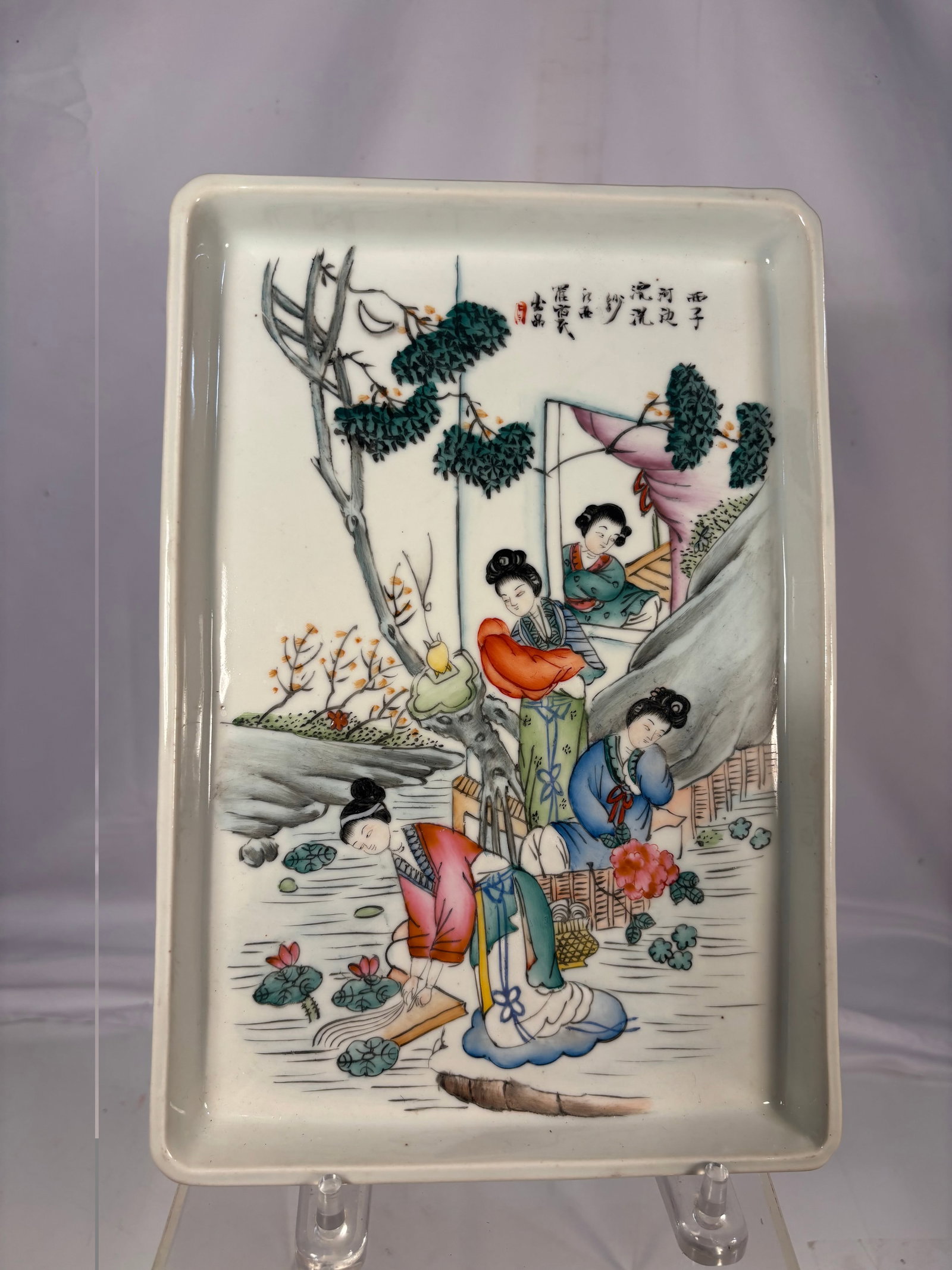A Chinese Famille Rose Porcelain Plaque Depicting Xi Shi Washing Silk , early 20 century: Chinese porcelain plaque finely painted in famille rose enamels depicting Xi Shi, the celebrated beauty of ancient China, accompanied by attendants in a garden setting. Inscribed with a poetic title a