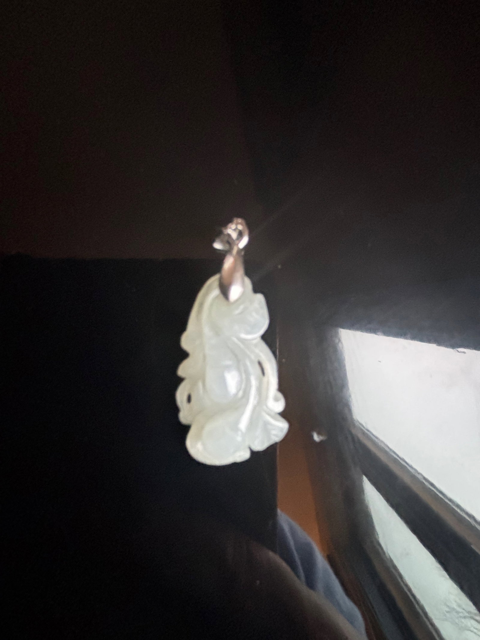 A Chinese carved Jade pendant: Qing Dynasty (1644-1912);This is a small, intricately carved nephrite jade pendant with a metal bale, designed for wearing as jewelry. The carving appears to depict a guard on leaf or a floral motif. 