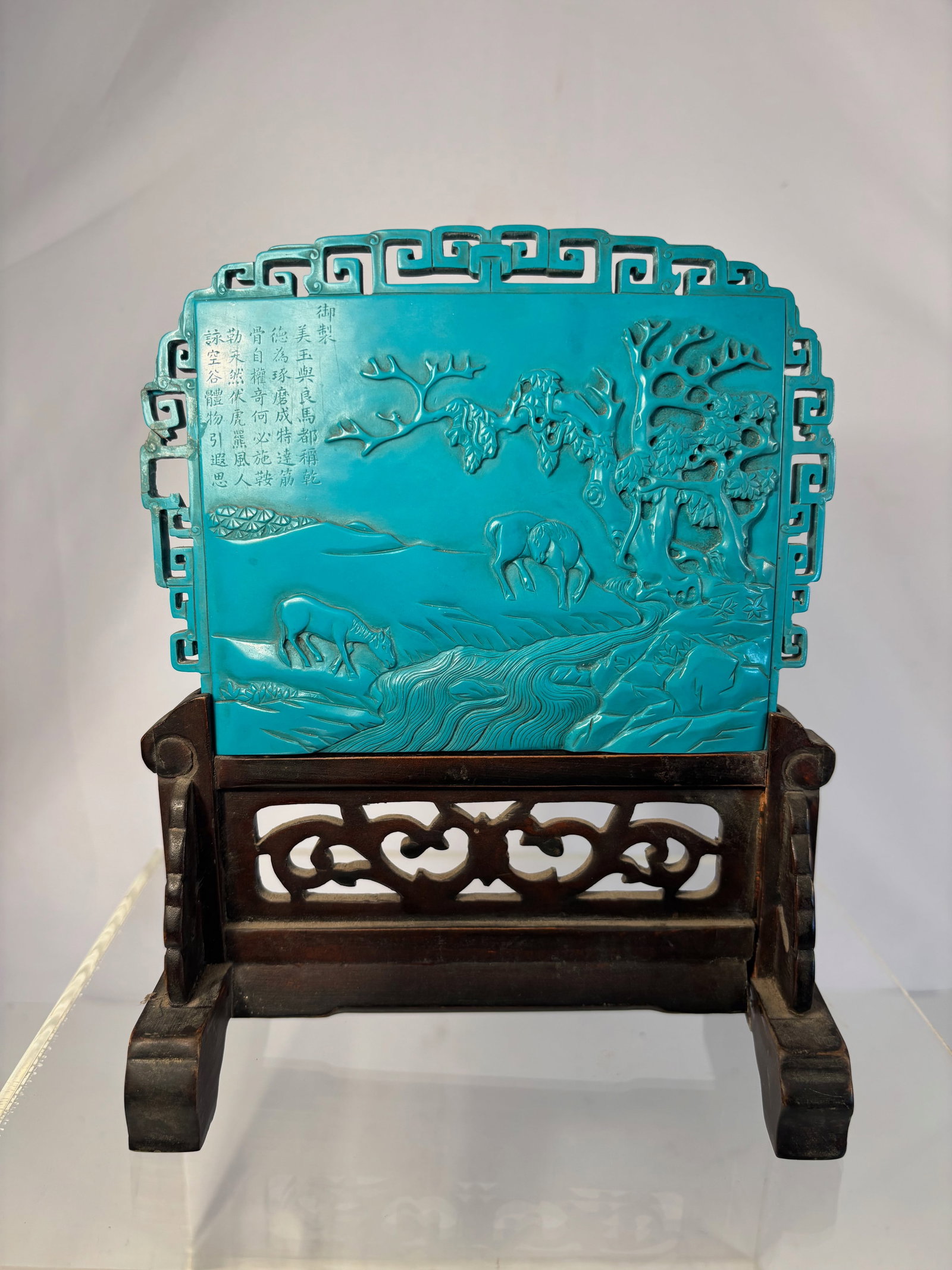 A Chinese imitation turquoise table screen panel, 20th century: Decorated in relief with two horses beside a river and trees, within a pierced key fret border, raised on a carved and pierced hardwood stand,The upper left is decorated with an engraved poetic inscri