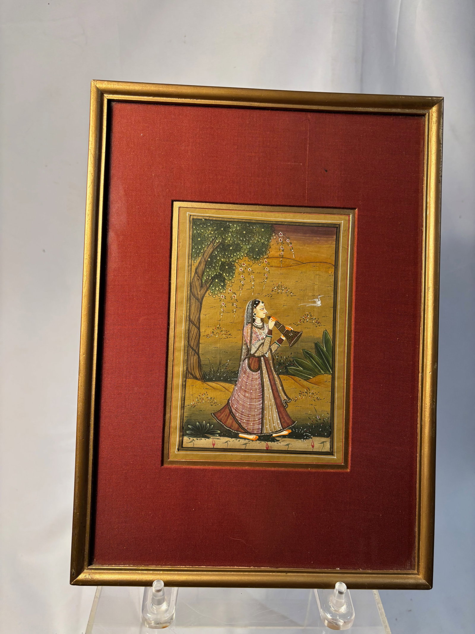 Indian Mughal Style Miniature Painting of a Lady Musician: Finely hand painted Indian miniature style painting depicting a court lady playing a traditional wind instrument in a garden landscape beneath a flowering tree. Executed in the Mughal / Rajasthani tas