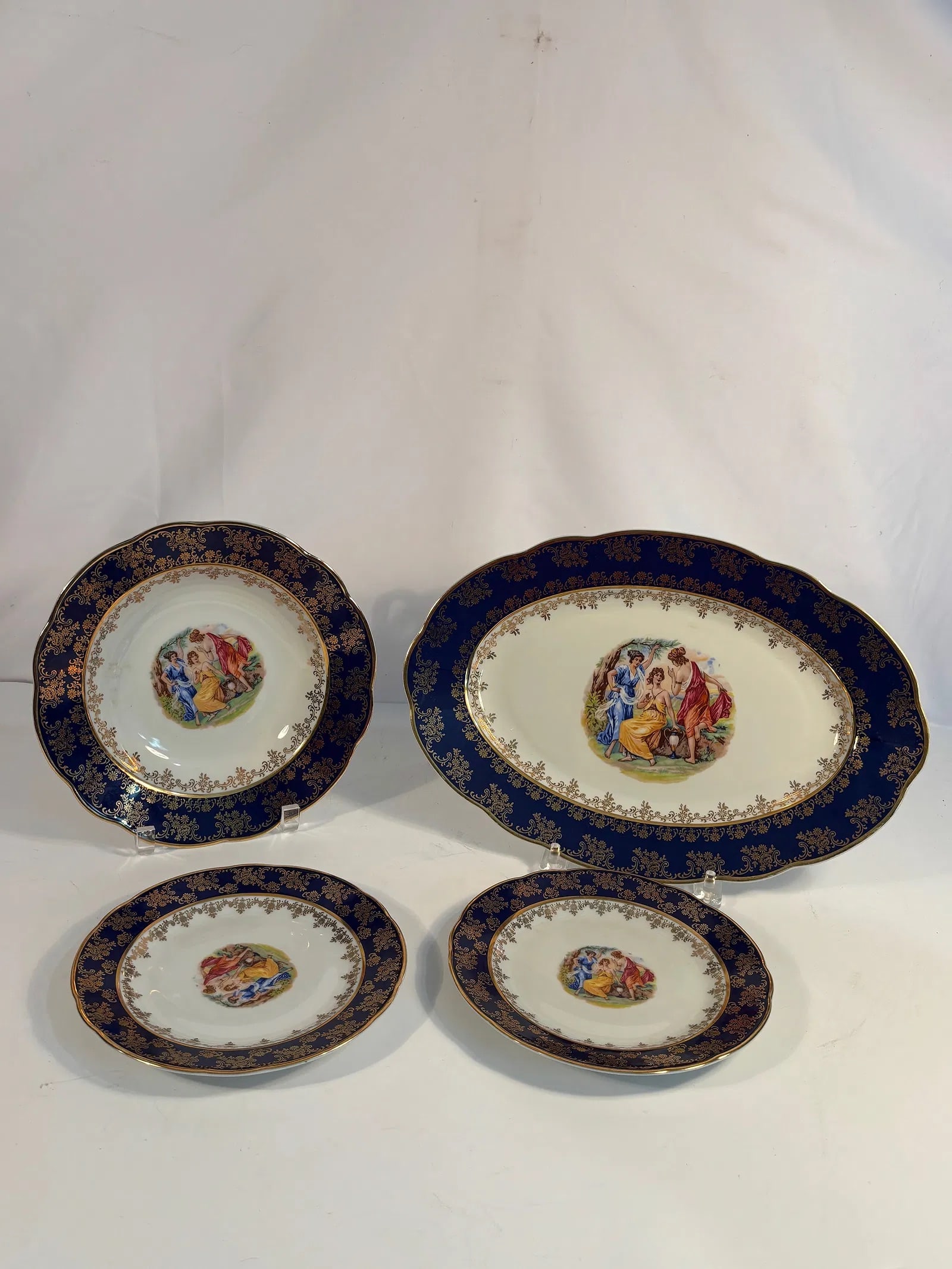 A Bohemia “Original Cobalt?? Gilt and Figural Porcelain Cabinet Set (4 pieces), Made in Czech: A fine group of cobalt-blue porcelain plates and serving dishes richly decorated with gilt foliate scrolls and central neoclassical scenes. Each marked Bohemia, Made in Czech Republic, Original Cobalt
