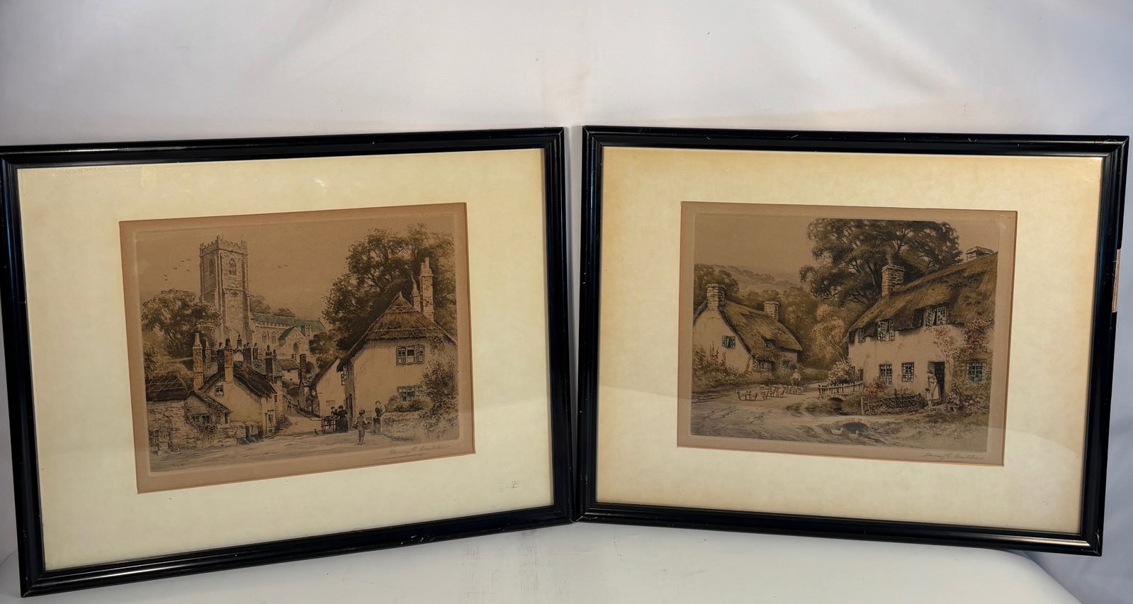 Henry G. Walker (British, early 20th century), “Cottages at Dunster?? and “Village Street,: Pair of original soft-ground etchings in color, each titled and credited on the reverse labels. Presented in matching vintage black lacquered frames with cream mats. Both works depict charming English