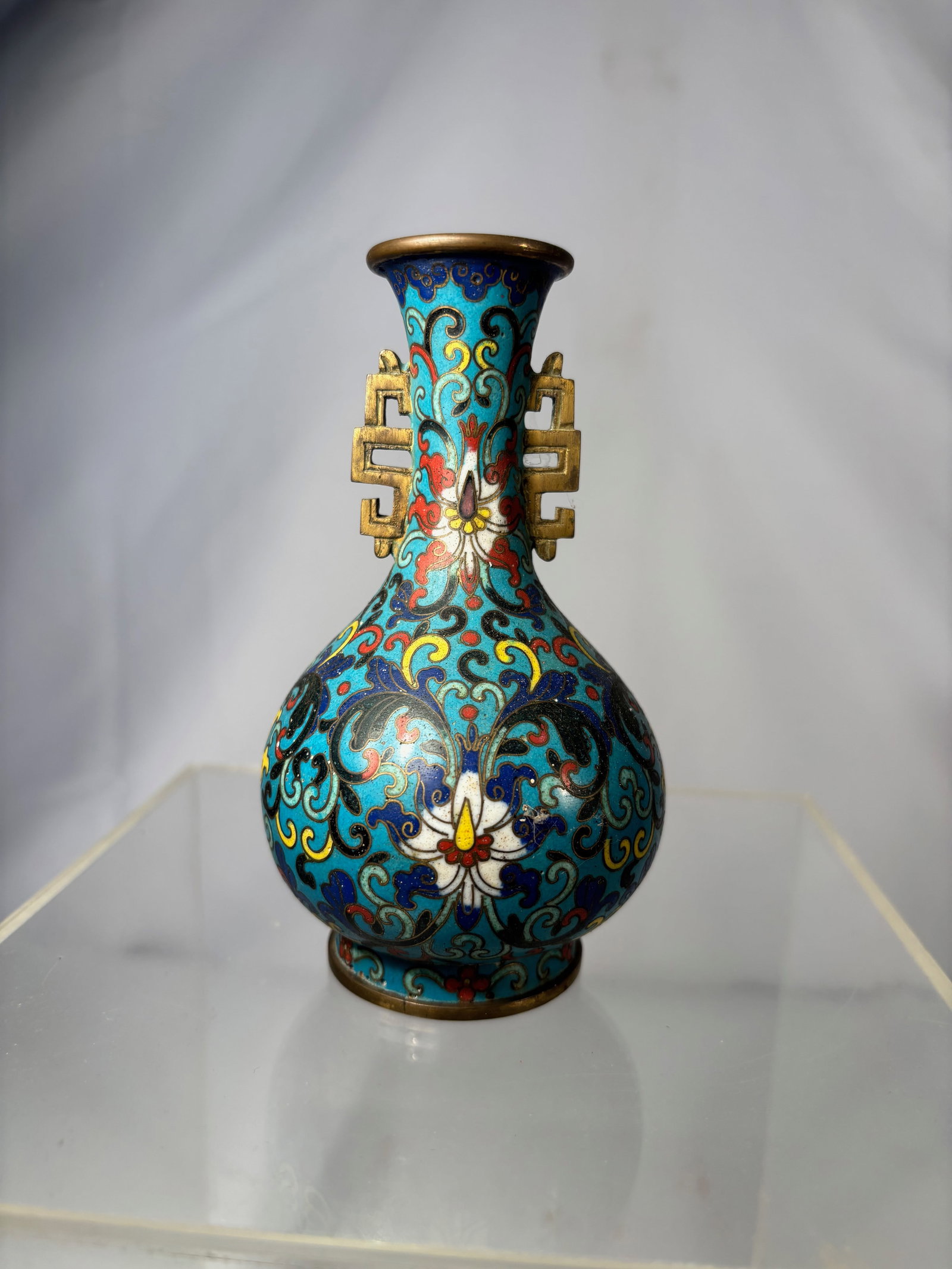 A Chinese Cloisonné Vase with Ruyi Handles, 18th- 19th centruy: Chinese cloisonné vase of baluster form, decorated with scrolling lotus and foliate motifs on a turquoise ground, executed in shades of blue, yellow, red, and white enamels. The neck fitted with a pa