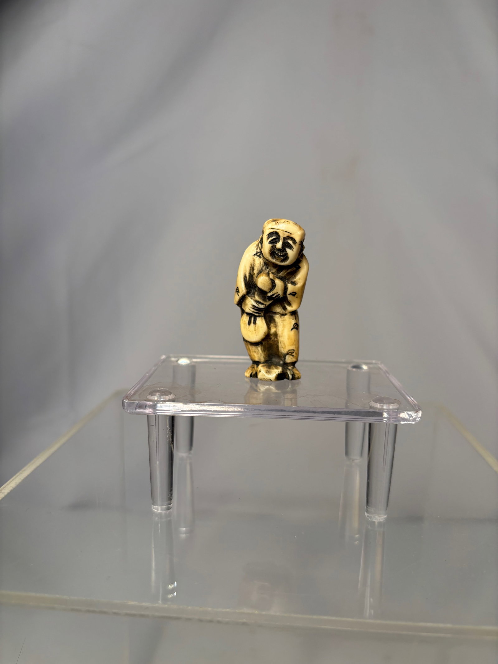 A Japanese Figural Netsuke, Carved Bone Standing Figure, Signed (Hisakazu / Ky?ichi): 19th century, A Japanese figural netsuke carved from bone, depicting a standing human figure with a humorous expression and stylized features. The carving includes two himotoshi to the reverse,