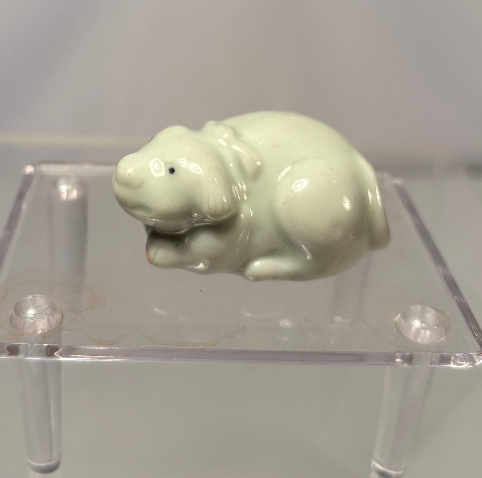 Hirado Porcelain Netsuke of a Shishi (White Lion-Dog), Japan, Meiji Period: Japanese Hirado porcelain netsuke depicting a shishi (mythical lion-dog), finely modeled in white-glazed porcelain with a compact crouching form and expressive features. The underside is pierced with 