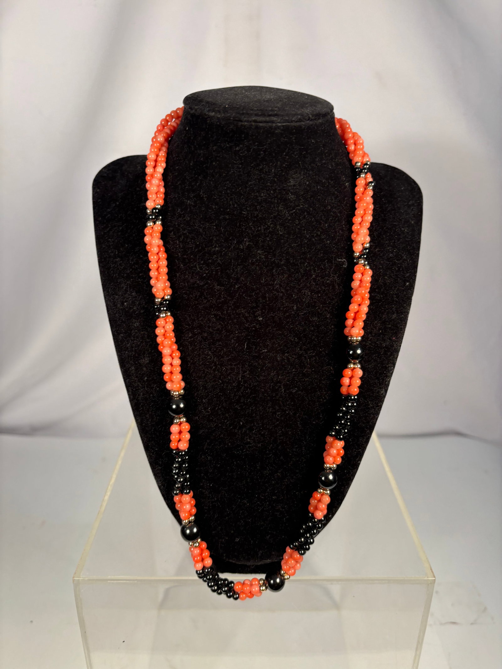 Vintage Long Triple-Strand Coral and Black Onyx Bead Necklace: A vintage long necklace composed of three strands of polished coral beads, accented with sections of small black onyx beads, larger round black onyx beads, and silver-tone spacers. Finished with a dec