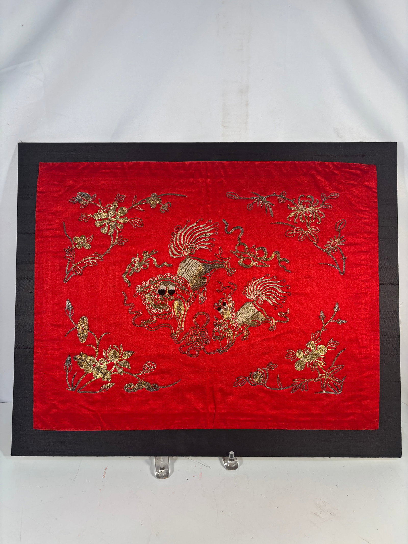 A Chinese Embroidered Red Silk Panel with Guardian Lions: Chinese embroidered silk textile panel featuring a vibrant red satin ground worked in metallic gold and polychrome thread with a central pair of guardian lions amid scrolling ribbons and surrounded by