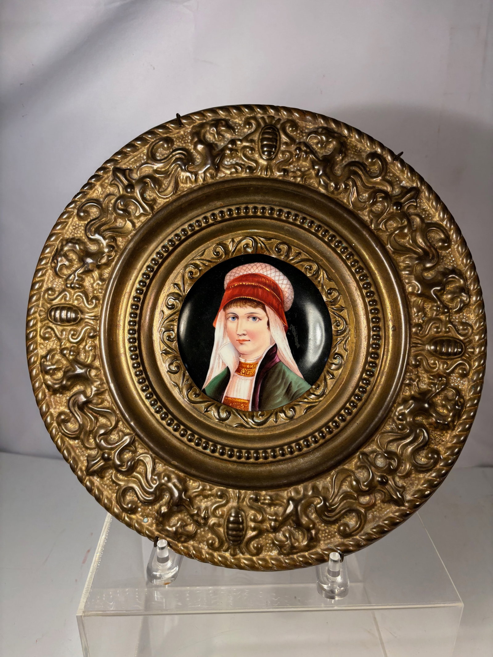 A European Hand-Painted Porcelain Portrait Plaque in Ornate Metal Frame: Likely late 19th to early 20th century, European hand-painted porcelain portrait plaque depicting a finely rendered female figure in historical attire, set against a dark ground. The miniature portrai