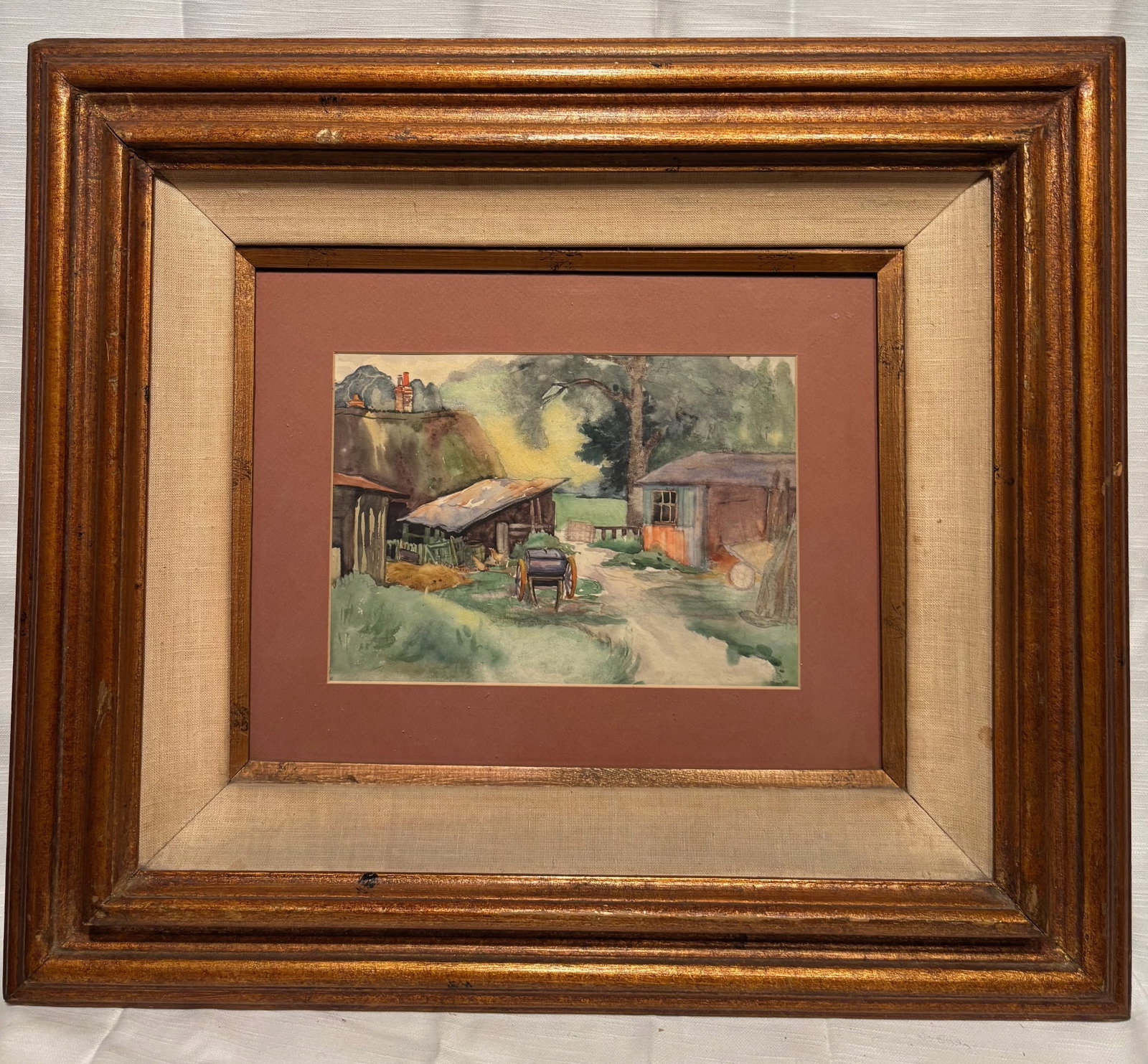 Rustic Country Farm Scene, Original Watercolor Painting, Framed Landscape: An original watercolor painting on paper depicting a rustic farm scene. The composition features a quiet rural setting with outbuildings, a dirt path, and a cart in the foreground, surrounded by trees
