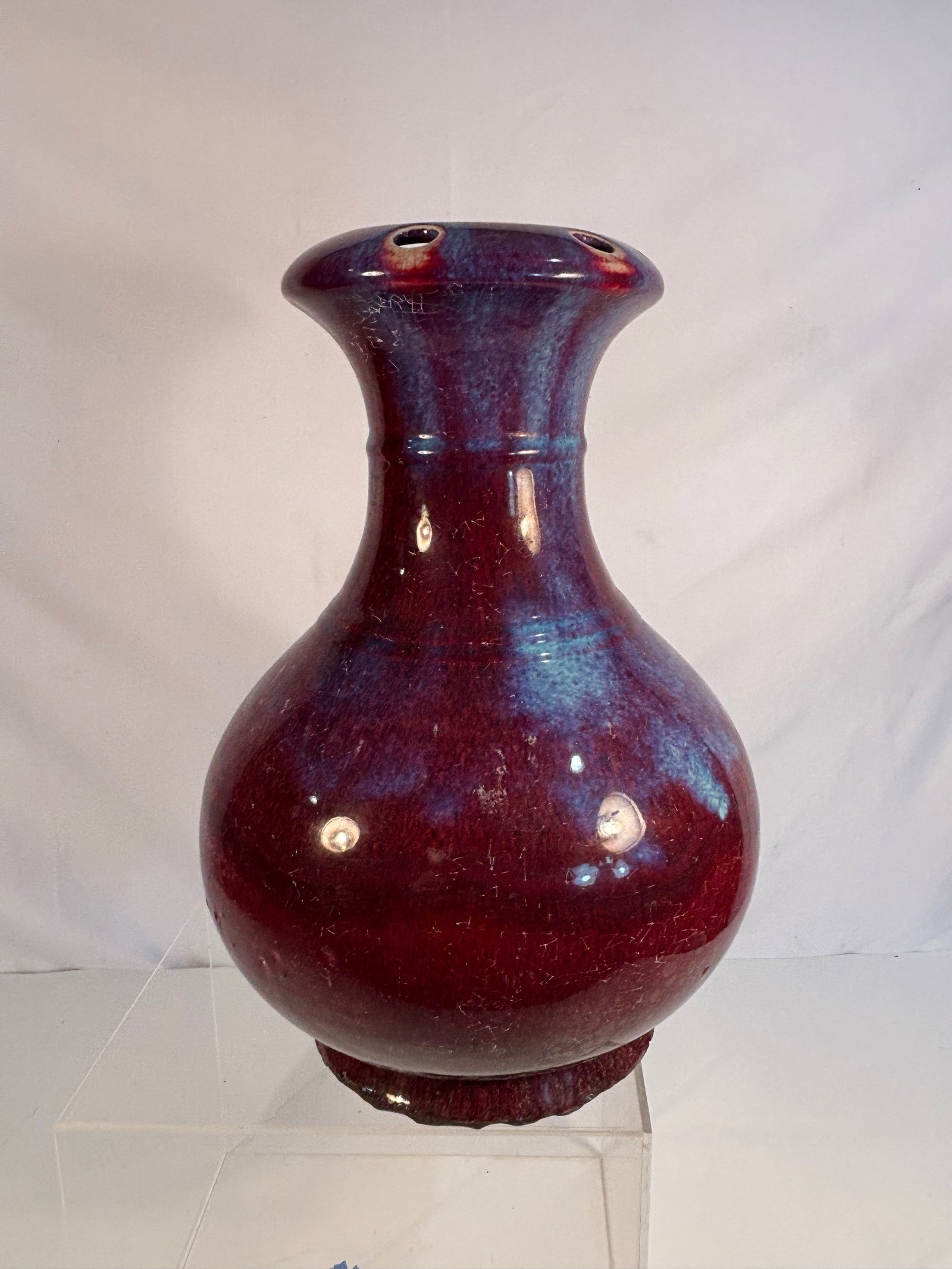 A Chinese Flambé-Glazed Porcelain Vase: 18th-19th century; Of bulbous body with a flared rim, the exterior covered in a rich glaze of deep crimson, streaked with violet and blue tones, thinning at the mouth to reveal multiple exposed spur m