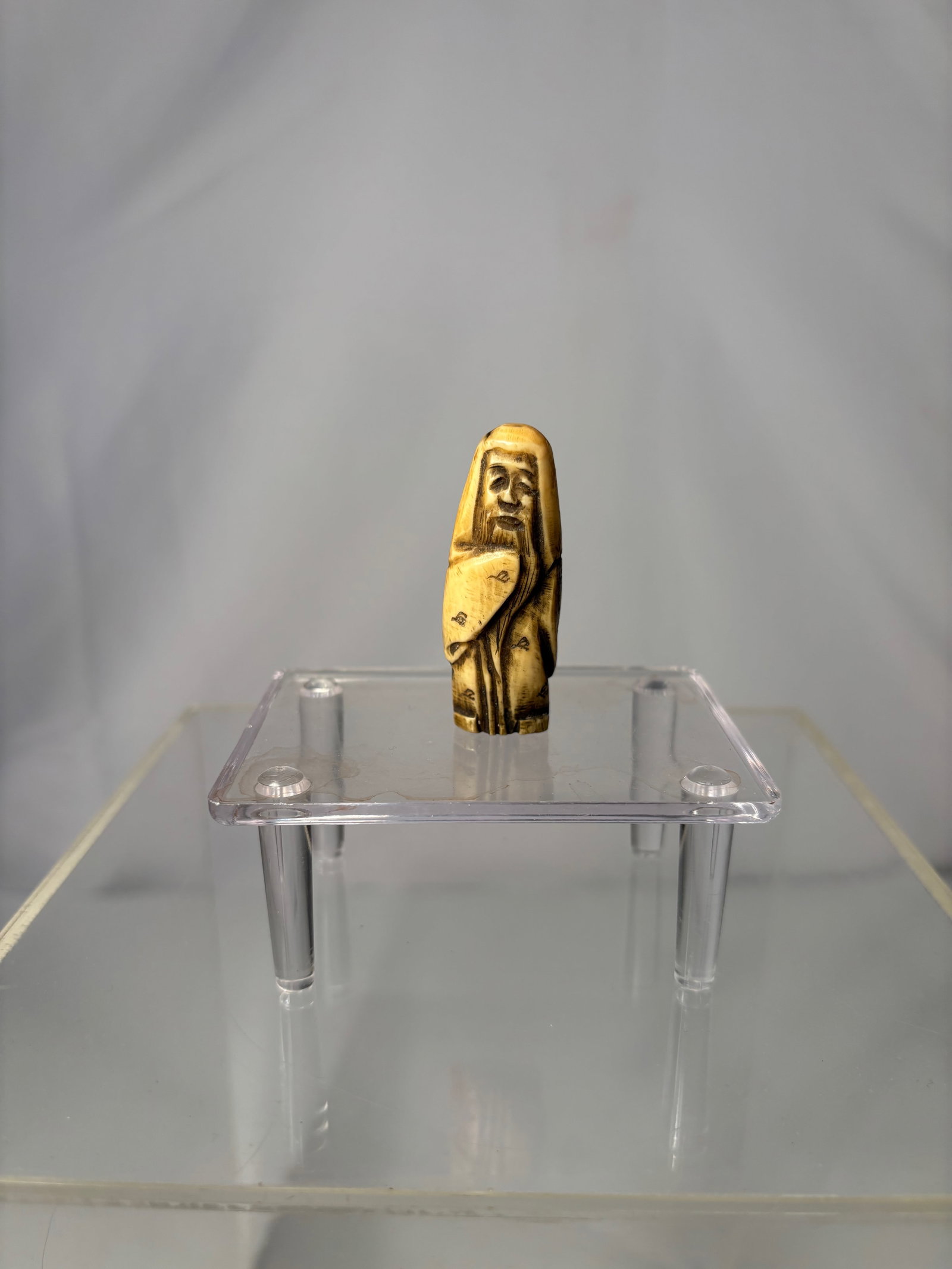 A Japanese Figural Netsuke, Carved Bone Standing Figure, Signed (Hisakazu / Ky?ichi): 19th century, A Japanese figural netsuke carved from bone, depicting a standing human figure with a humorous expression and stylized features. The carving includes two himotoshi to the reverse,