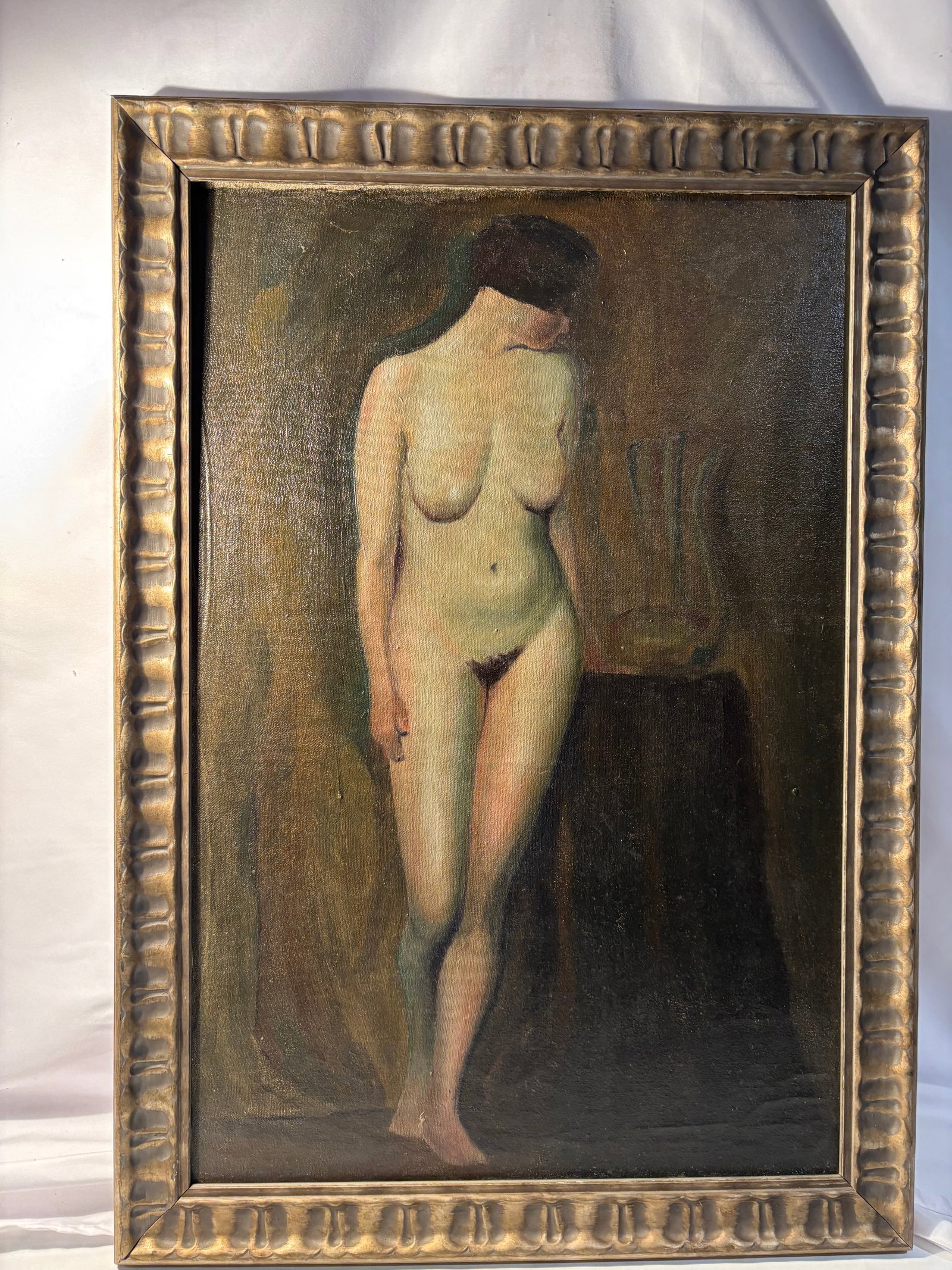 Modernist Nude Oil Painting: Unsigned oil on canvas depicting a standing female nude beside a table and vase. Executed in a subdued modernist palette with stylistic. Housed in a period frame. Frame Size: 27 X 19 in.