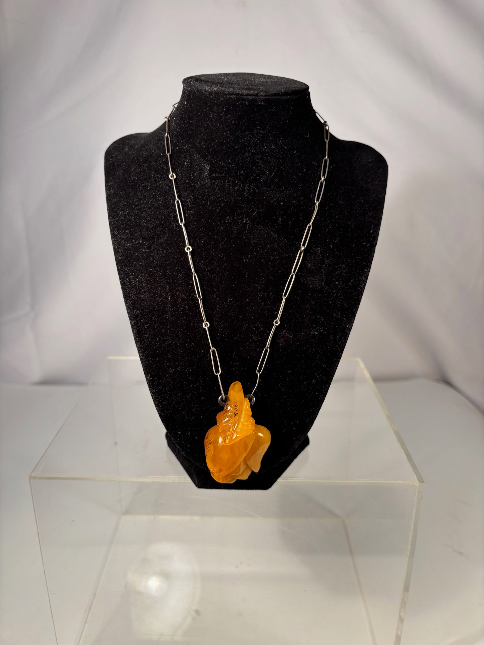 A Butterscotch Amber Carved Pendant on Silver-Tone Chain: This necklace features a carved butterscotch amber pendant, displaying a rich opaque yellow to warm honey tone characteristic of classic butterscotch amber. The pendant is carved in an organic, sculpt
