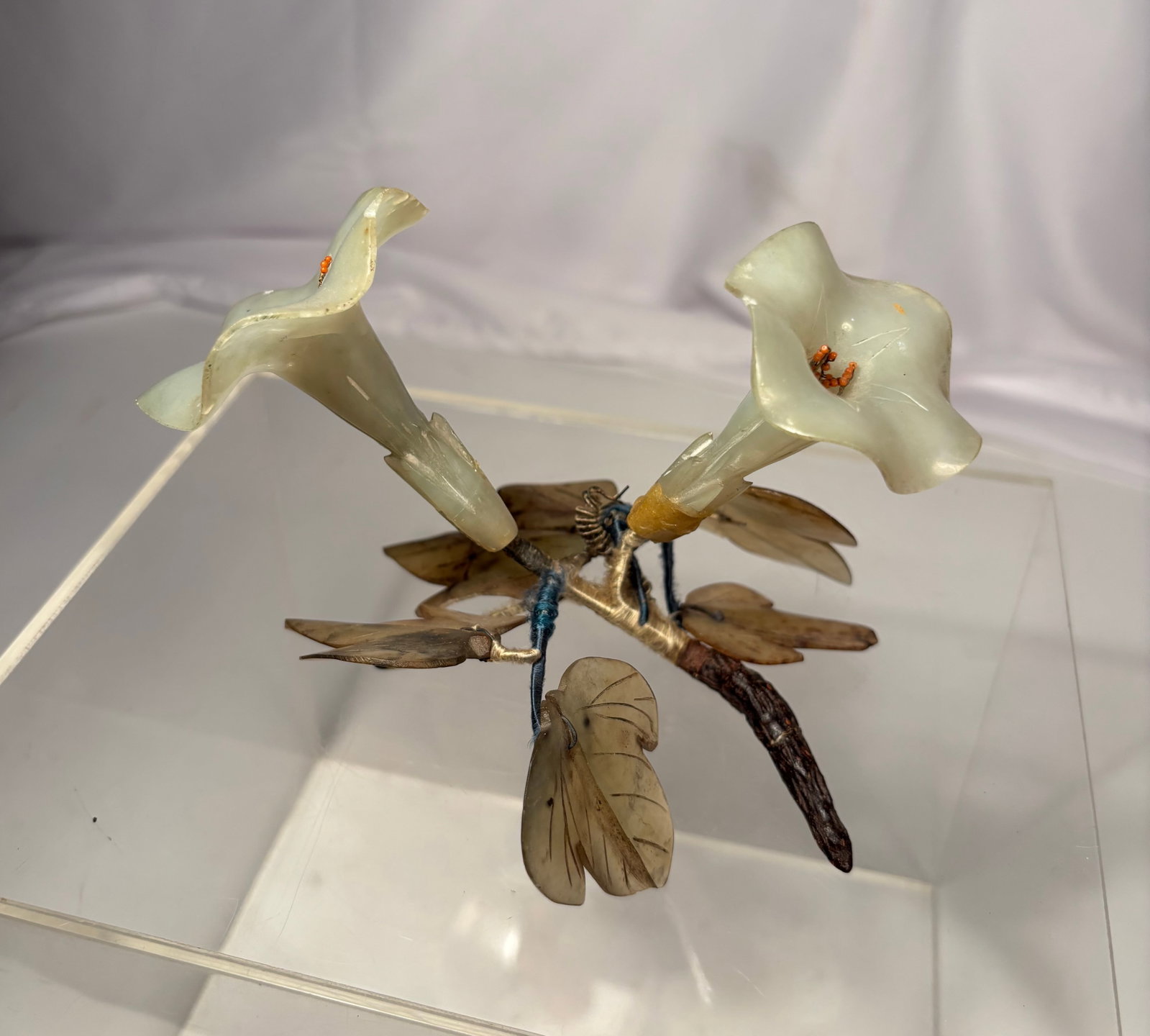 A Chinese Carved Jade and Coral Calla Lily Brooch Circa 1900–1920: A Chinese carved jade brooch depicting two elegant calla lily blossoms with carved jade leaves mounted on a naturalistic metal stem. The flowers are accented with coral bead stamens, enhancing the del