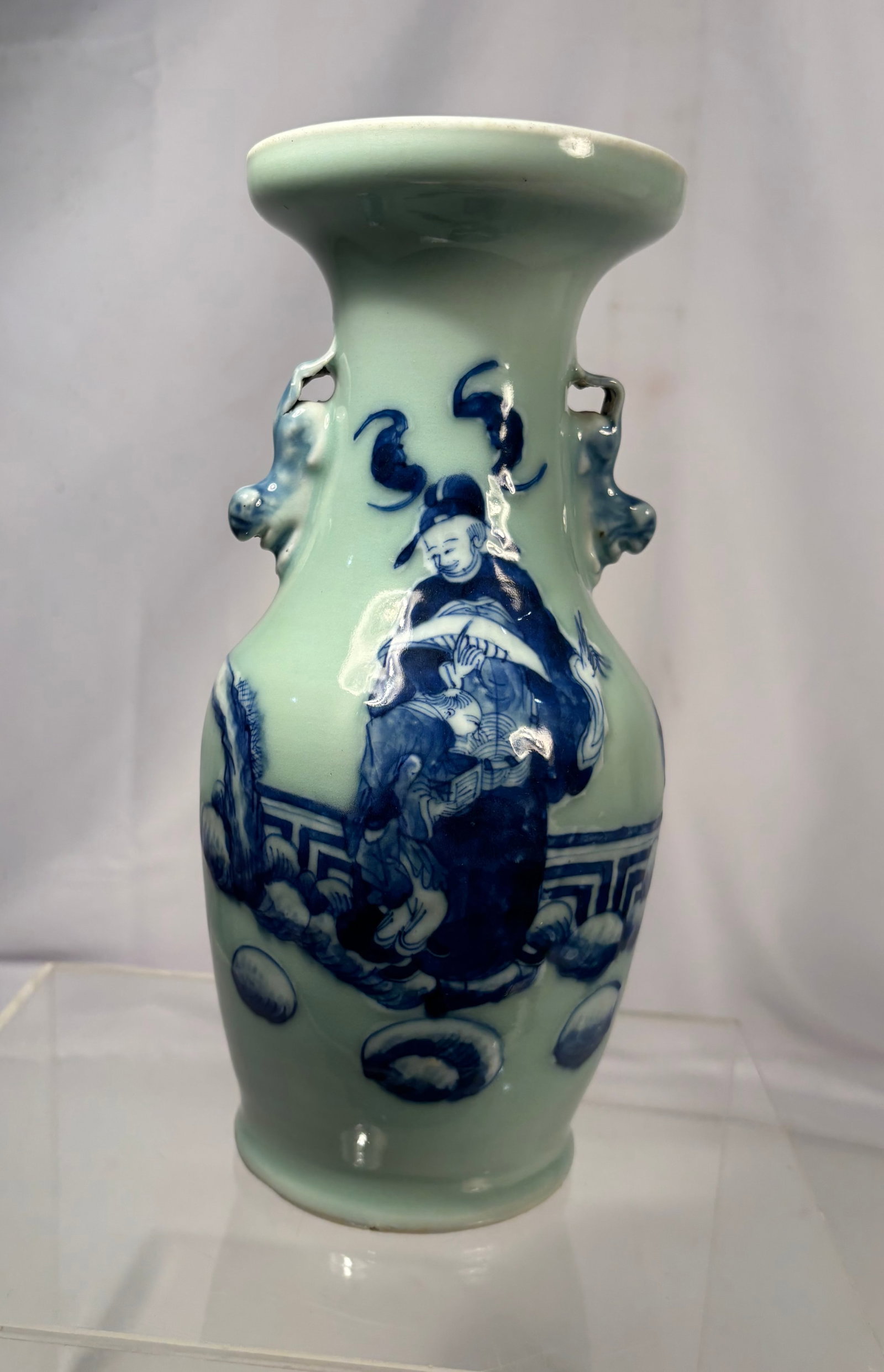 A Chinese Celadon Glazed Porcelain Vase with Blue and White Scholar Decoration 19th Century: A Chinese celadon-glazed porcelain vase of baluster form with a flared trumpet rim. The body is decorated in underglaze cobalt blue depicting a seated scholar in a garden landscape, accompanied by sty