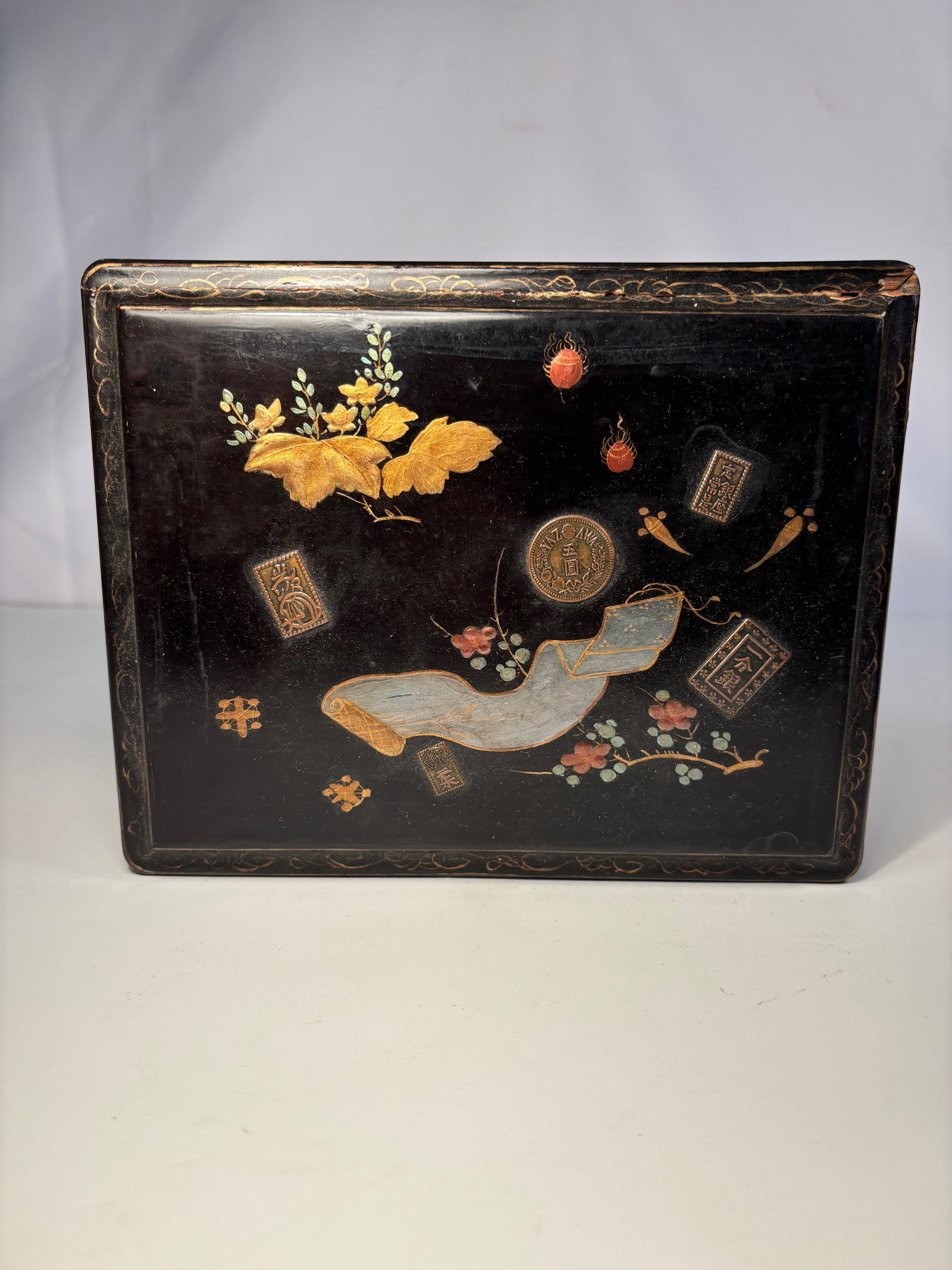 A Japanese Meiji Lacquer Suzuribako with Gold Maki-e and Raden Inlay, c.1900: Meiji (1868–1912); Rectangular form with a hinged lid, finely decorated in gold and silver hiramaki-e and takamaki-e lacquer on a black ground with scrolls, auspicious coins, and flowering branches,